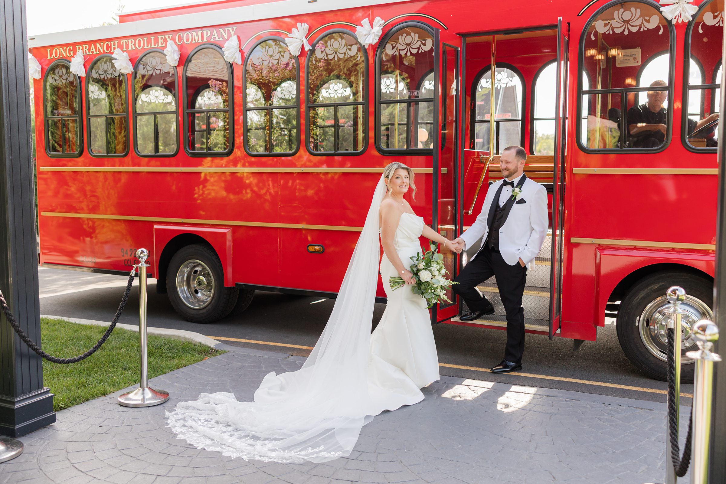 Bride and groom hold hands beside a vibrant red trolley, sharing a joyful moment as they step into their newly married life together