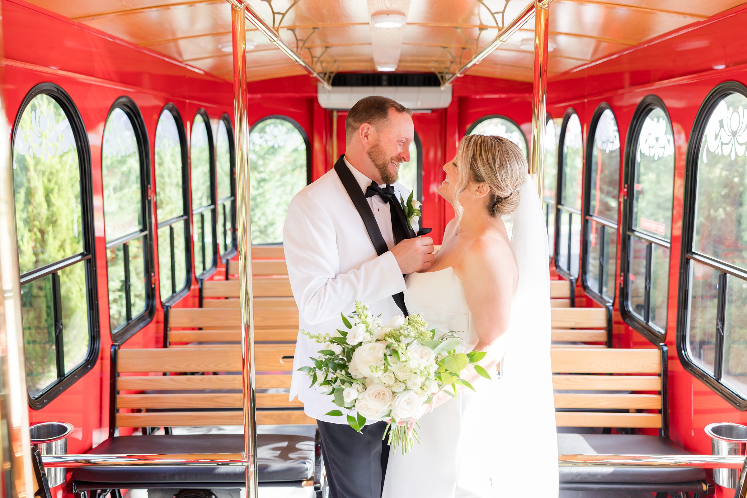 Bride and groom share a quiet, intimate moment inside a bright red trolley, smiling at each other as they embrace their first moments as newlyweds