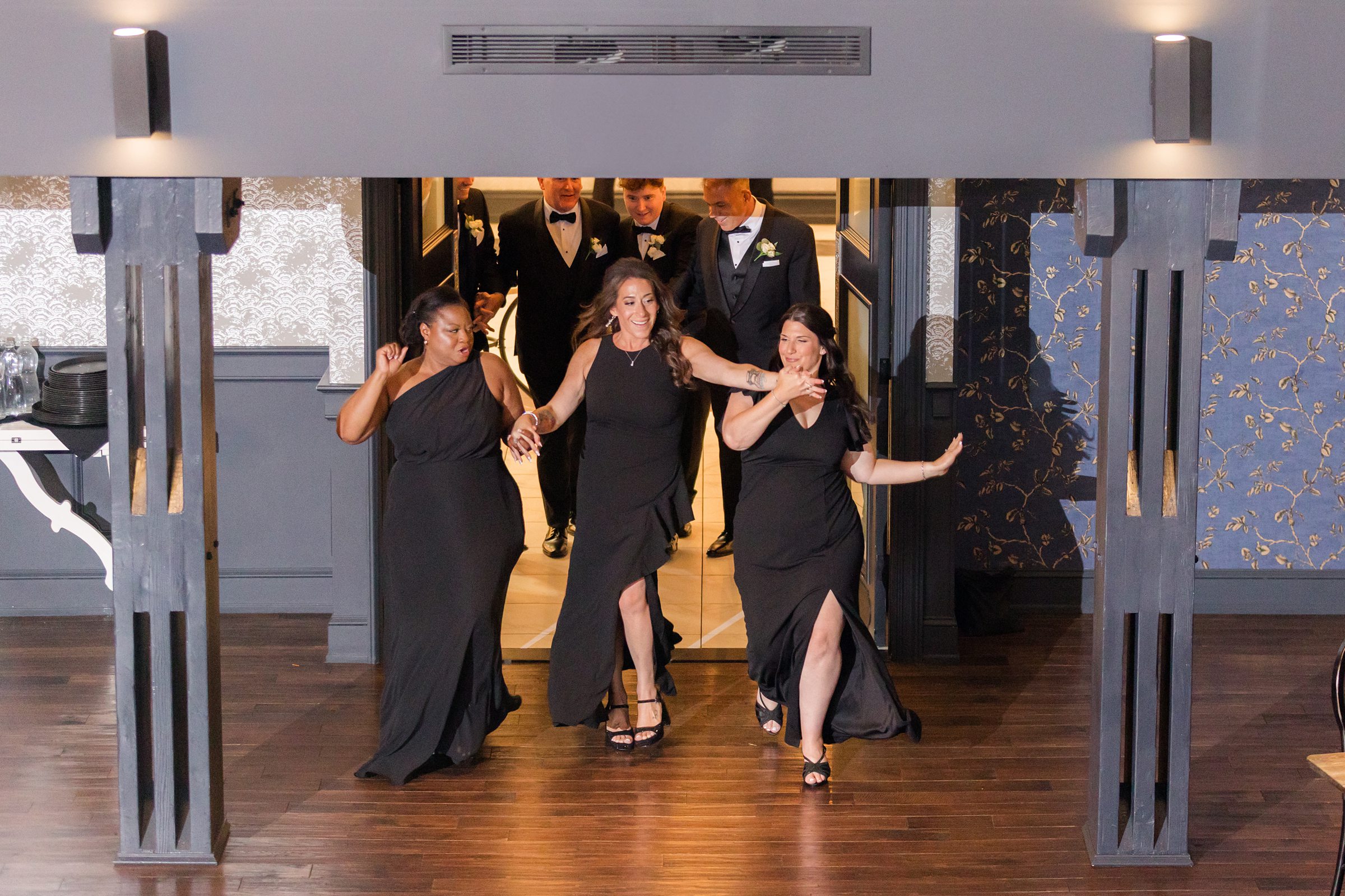 Bridesmaids and groomsmen burst into the room with energy and laughter, kicking off the celebration