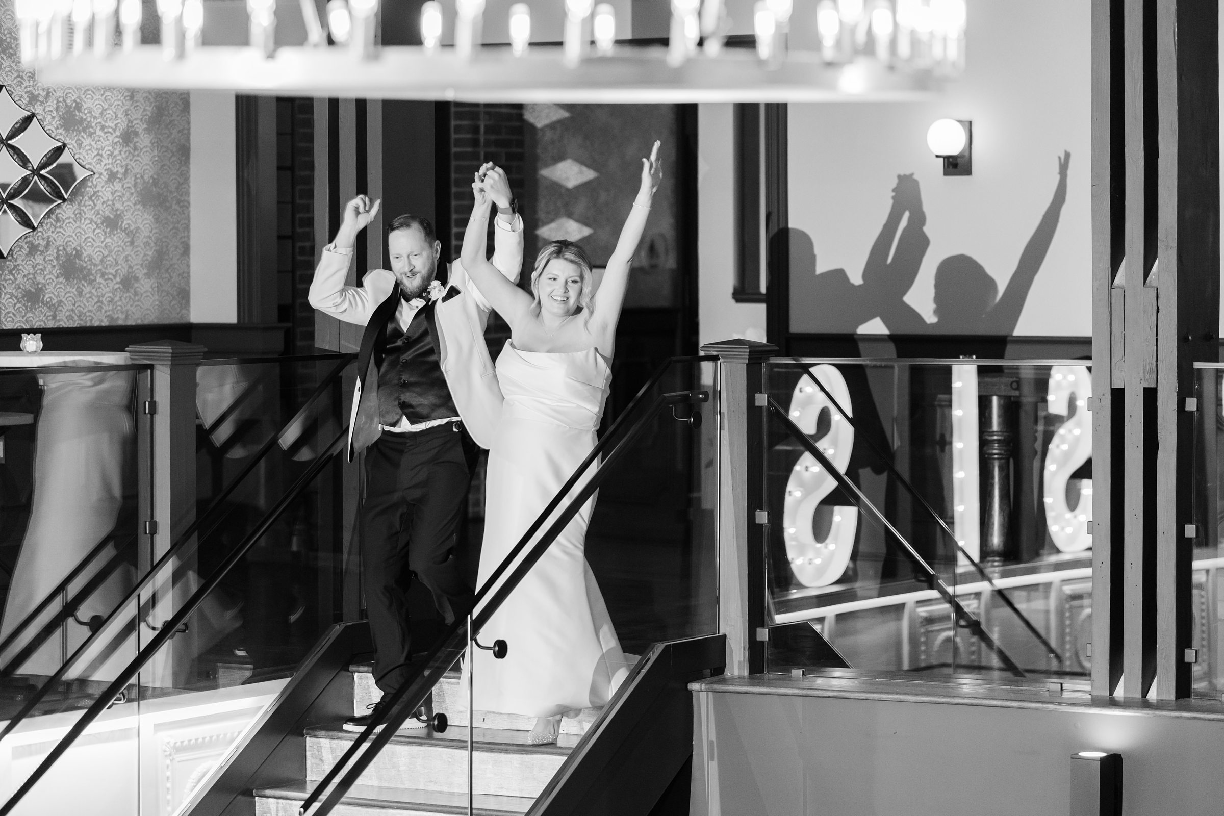 Bride and groom step down together in timeless black and white, lifting their hands in pure joy as they celebrate their first moments as newlyweds.