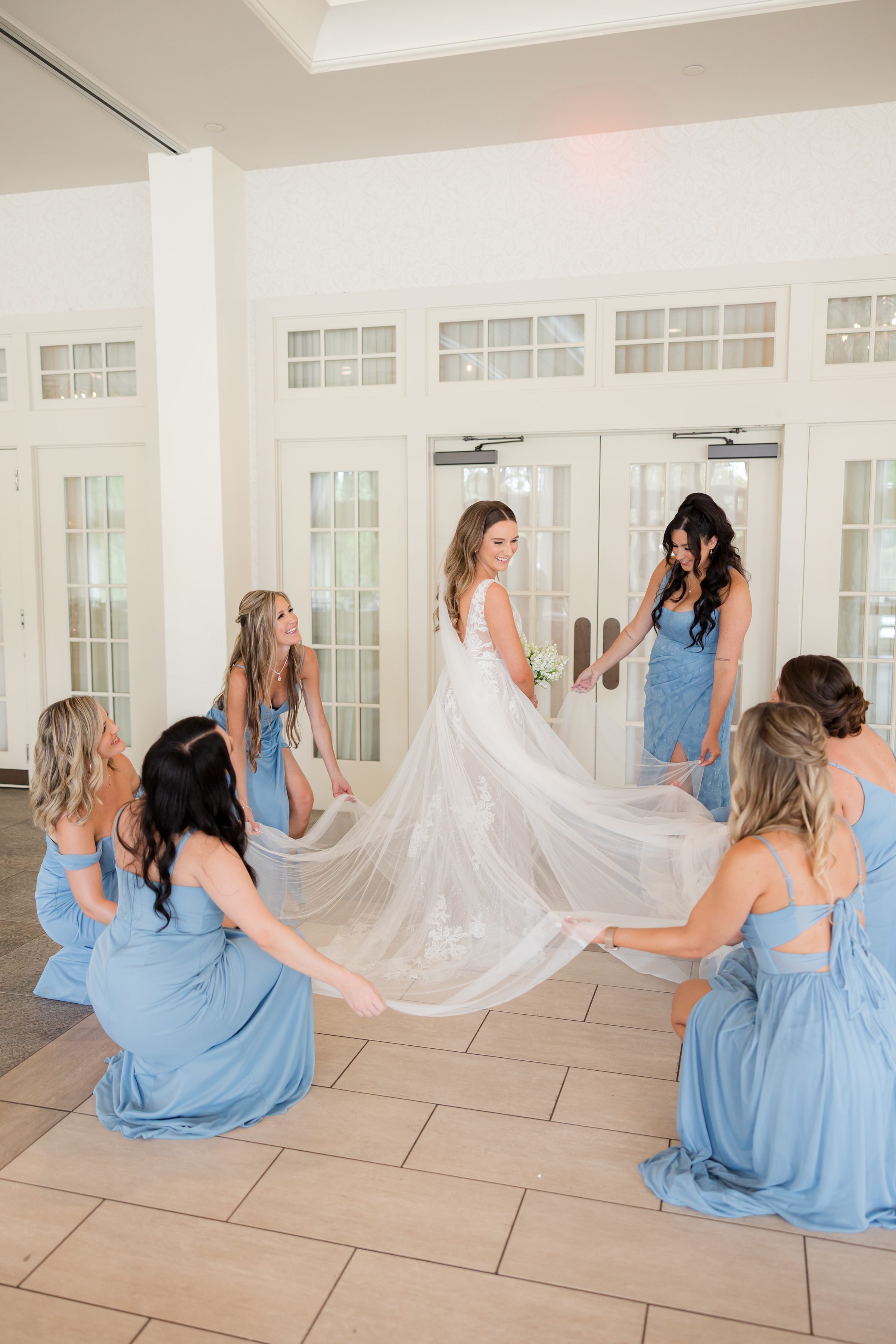 Bridesmaids gather around the bride, lifting her gown with laughter and admiration, sharing in her joy