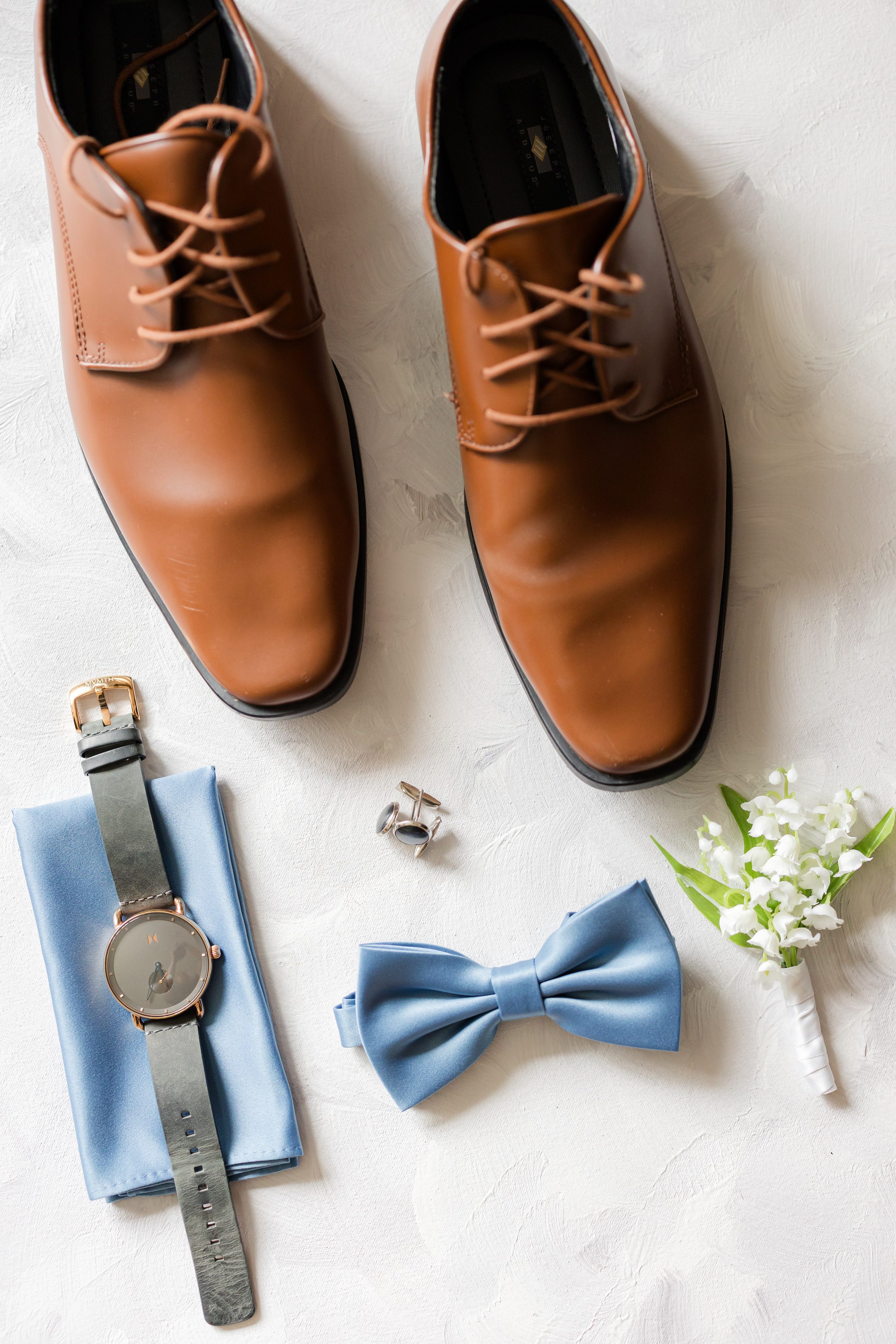 Polished leather shoes, a delicate blue bow tie, and meaningful details come together in a quiet still life, capturing the groom’s timeless style and the excitement of the day ahead