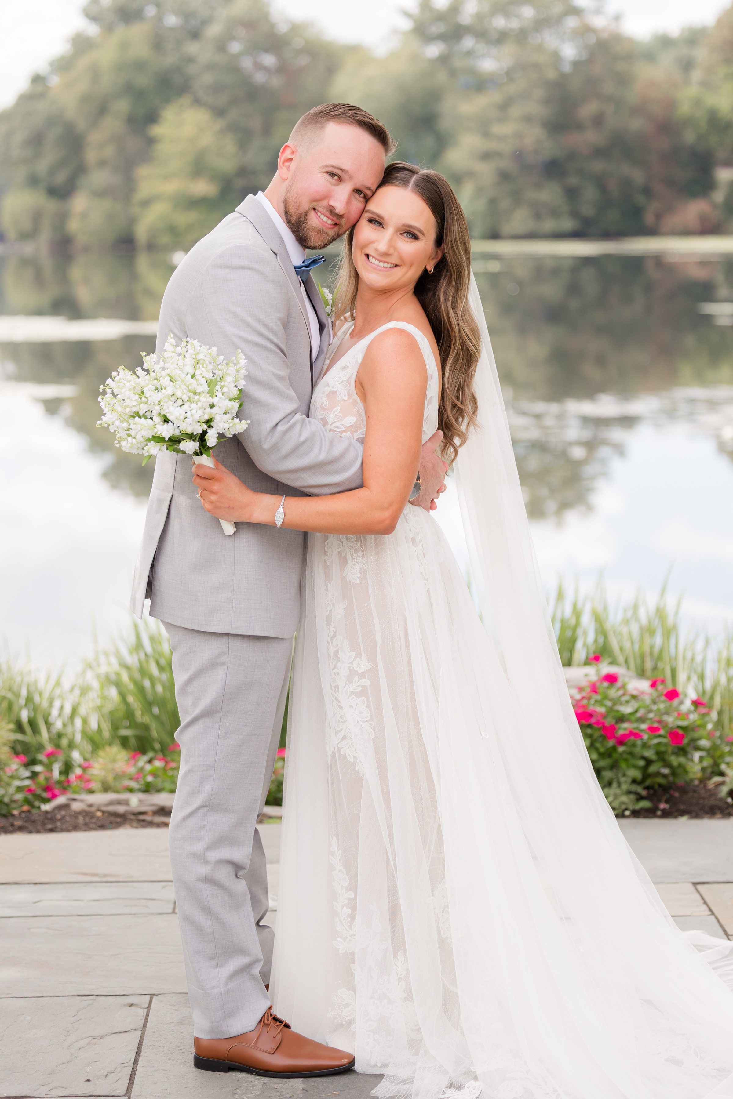 Bride and groom hold each other close by the water’s edge, their smiles soft and full of love as they begin their foreve