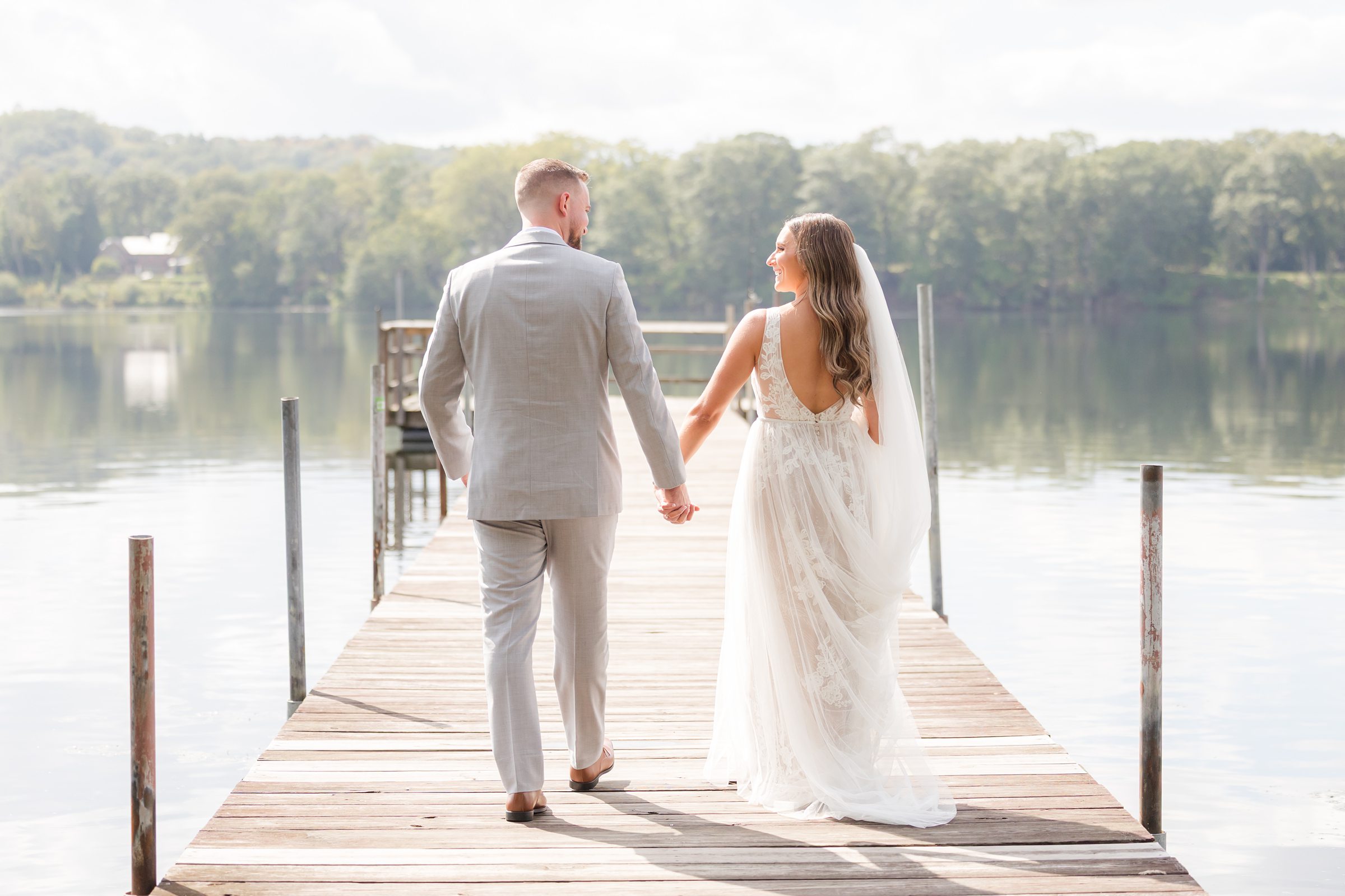 Groom walk together along the dock, their reflections shimmering in the still water as they step into a future filled with love and quiet devotion