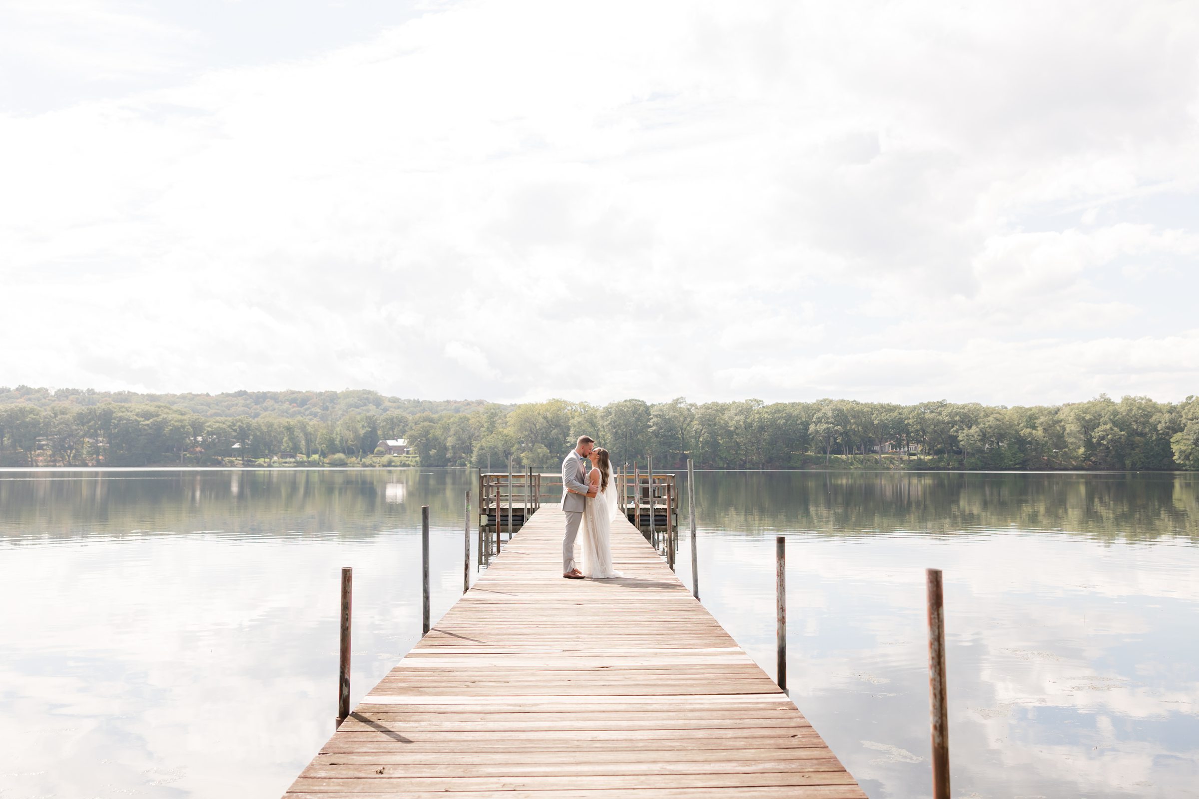 Bride and groom share a tender kiss, wrapped in still water and soft sky, as the world fades away and only their love remains