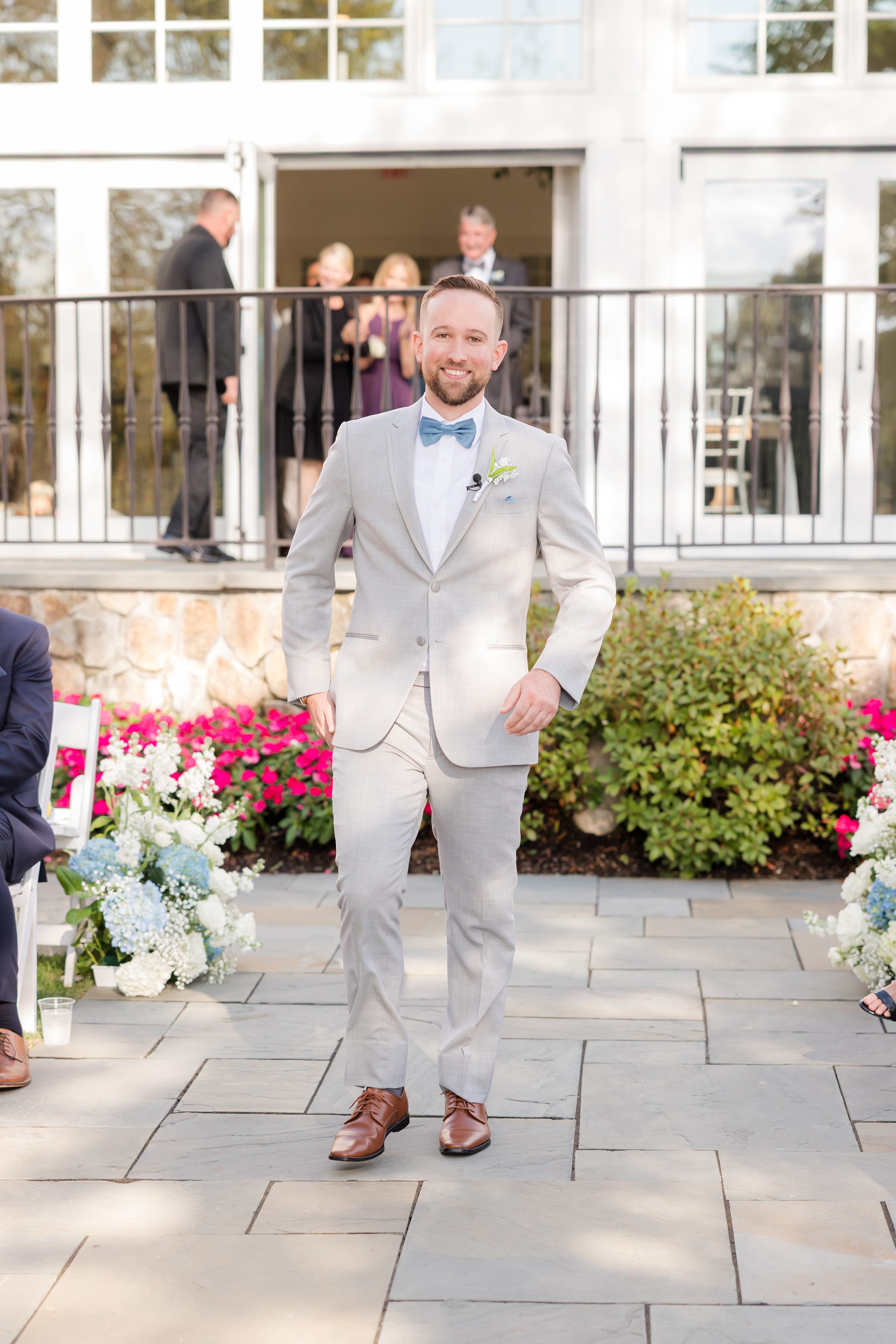 Groom stands confidently in a light gray suit, waiting with anticipation, surrounded by soft florals and the warm glow of the wedding day