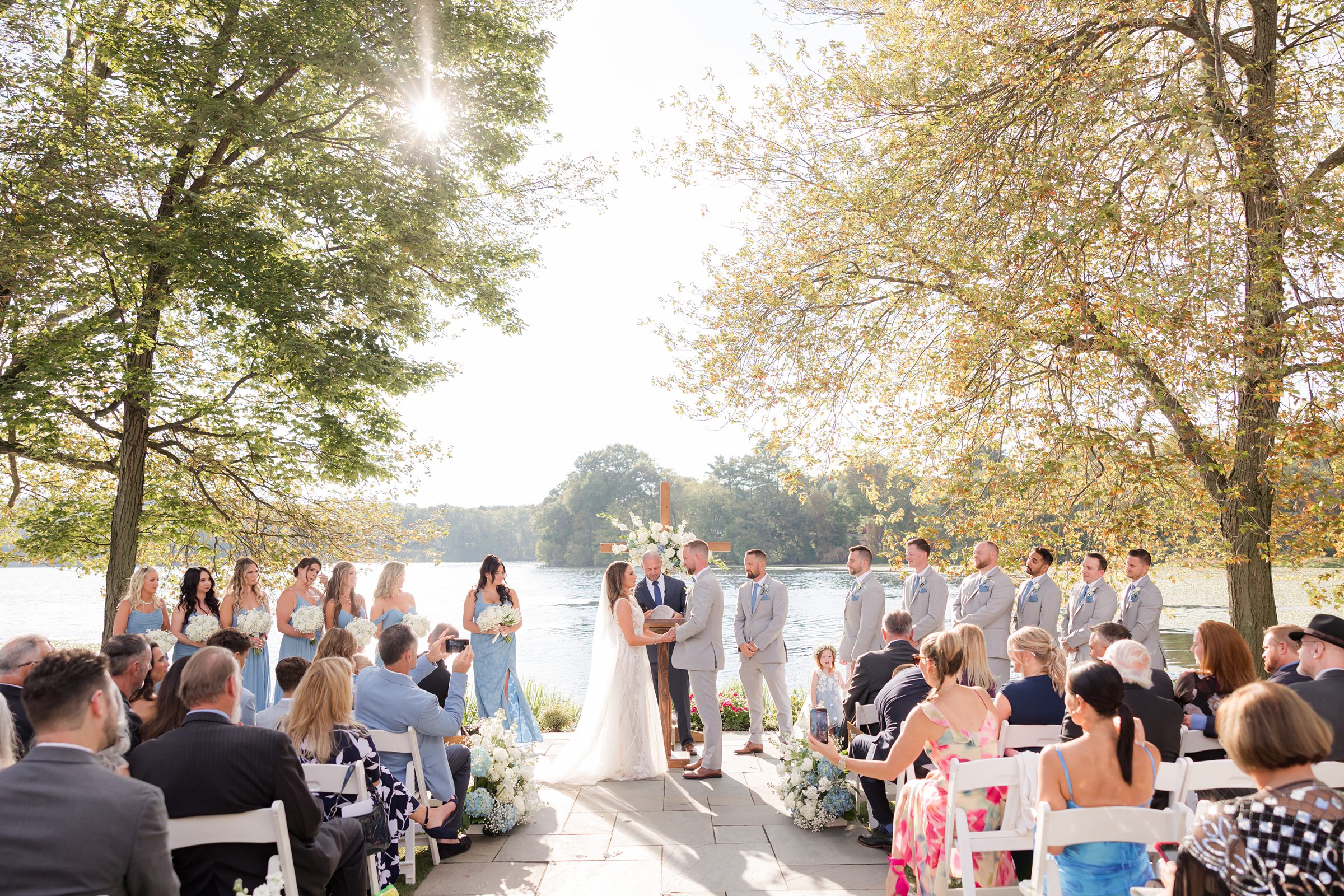 Bride and groom exchange vows, then lean into a tender embrace, surrounded by soft sunlight, blooming florals, and loved ones witnessing their moment
