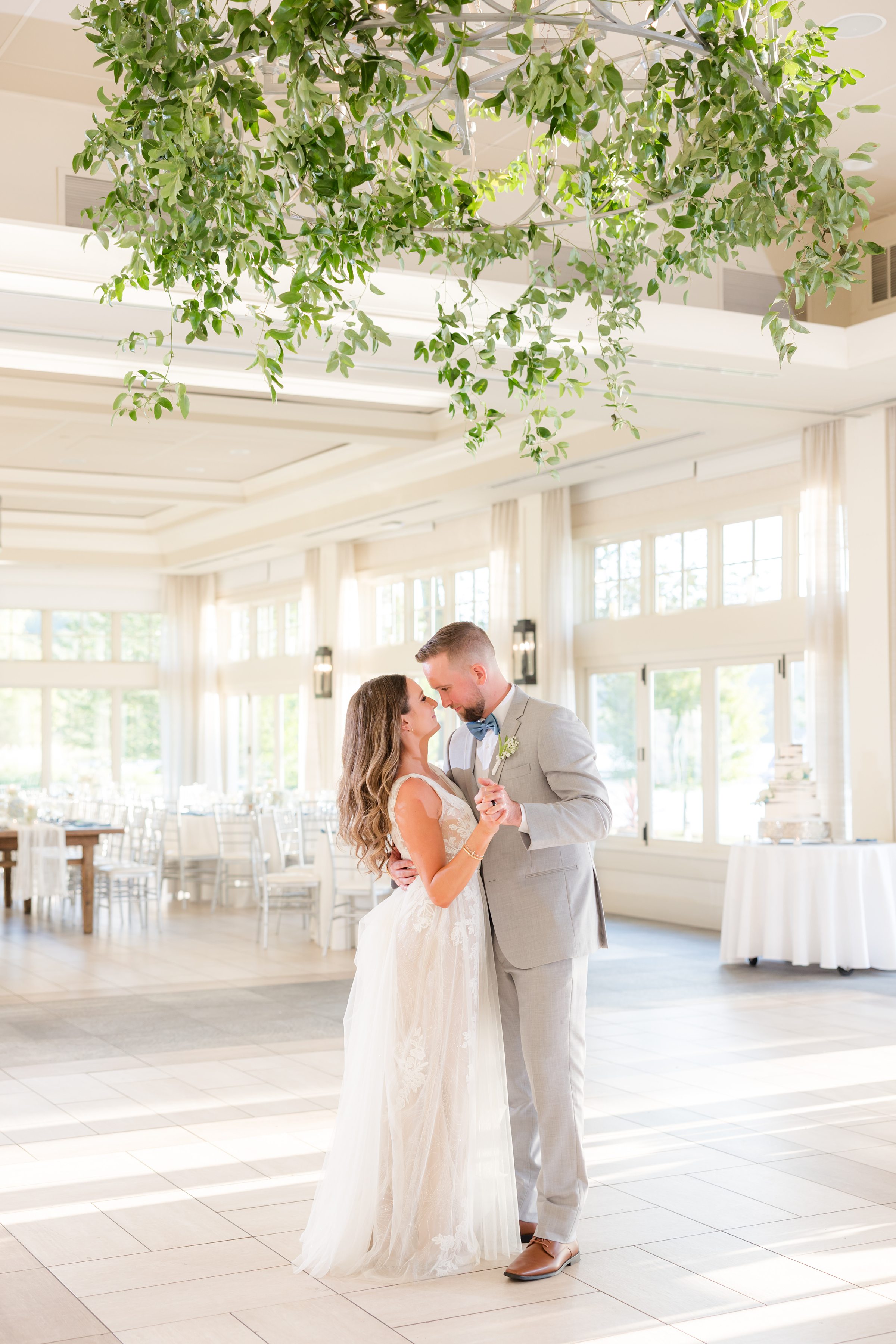 Bride and groom embracing in a sunlit reception space, surrounded by soft natural light and greenery overhead