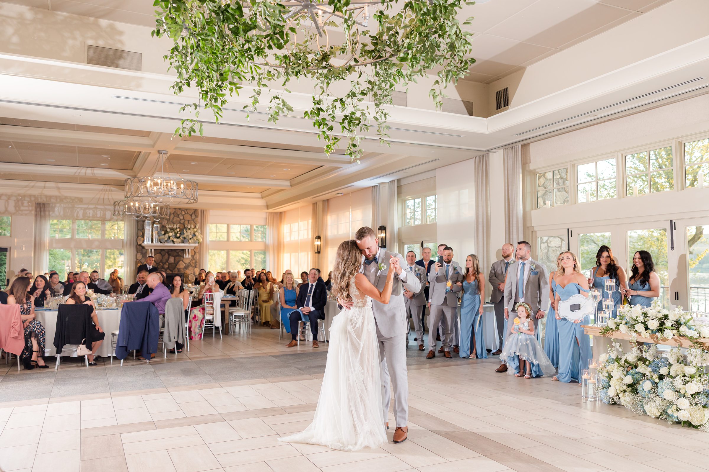 Sunlit hall, the couple dance at the center of a room filled with family and friends watching with joy