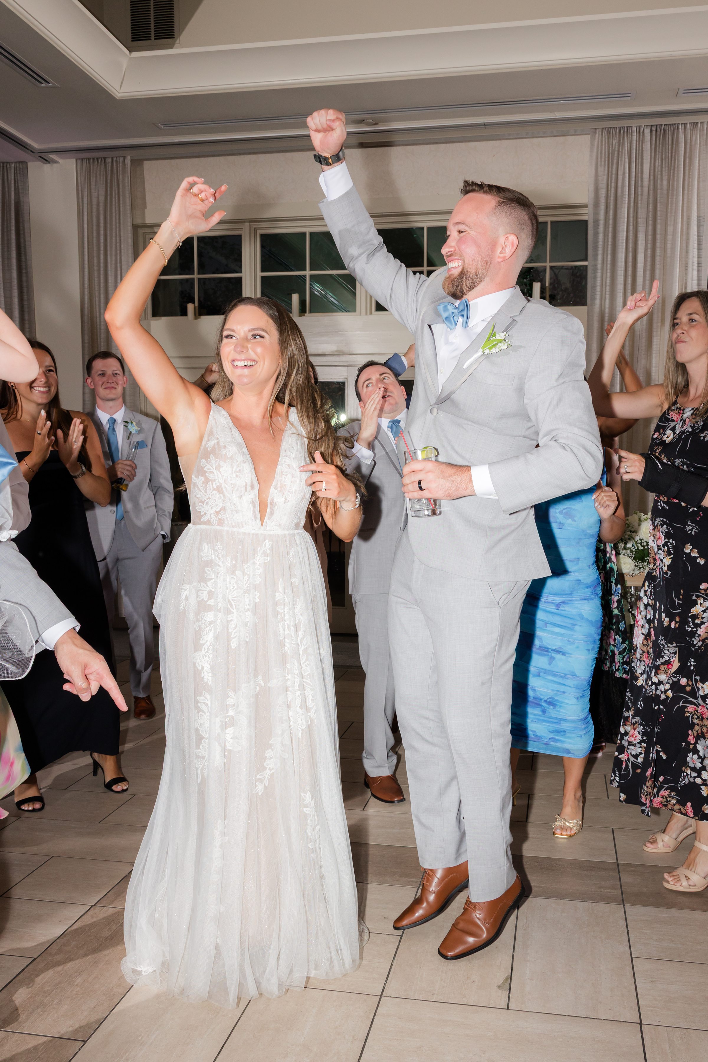 Bride and groom lift their hands in celebration, surrounded by cheering guests as their love fills the dance floor