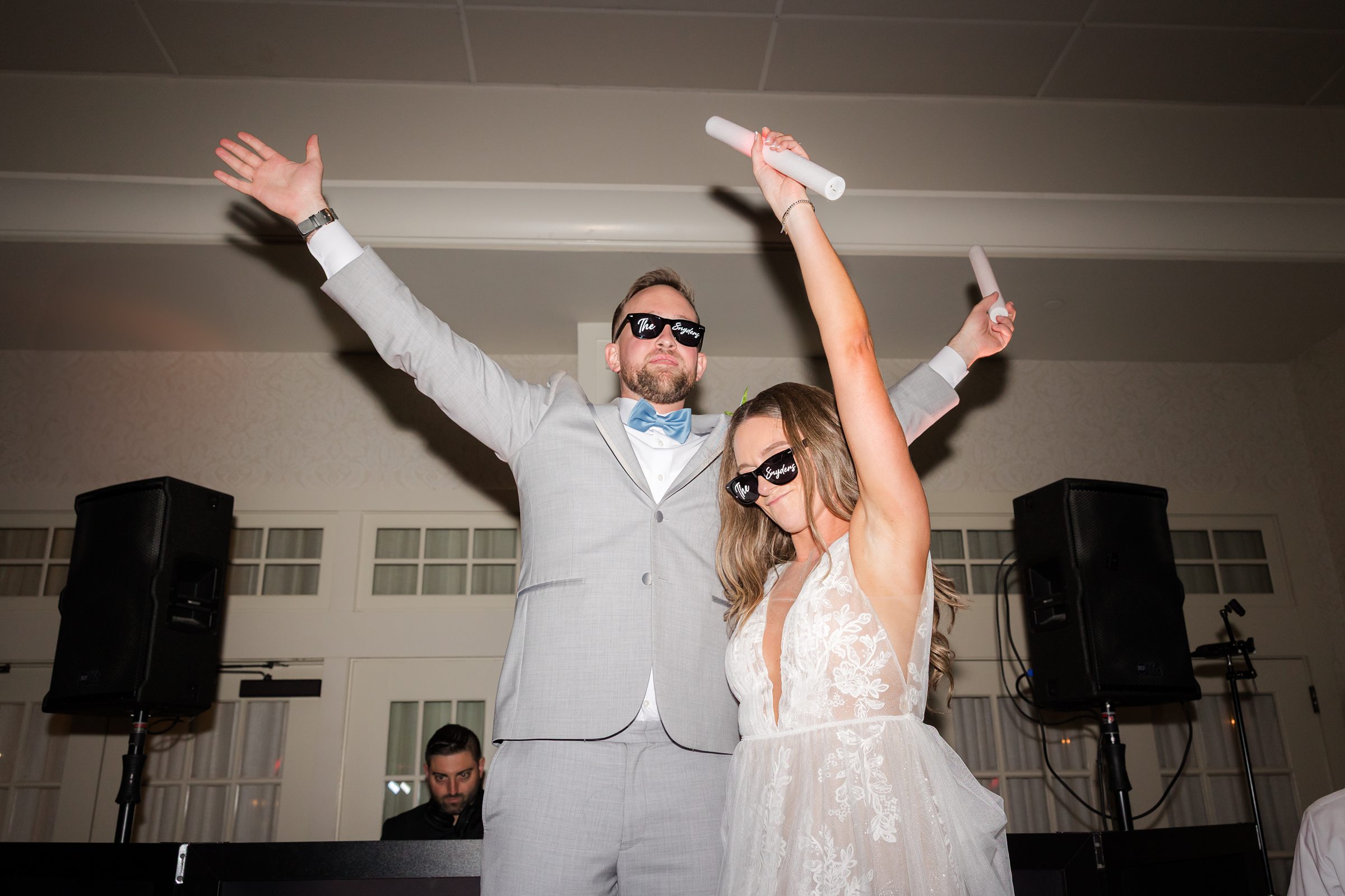 Groom dances playfully with glowing sticks while the bride laughs beside him, their carefree energy filling the room