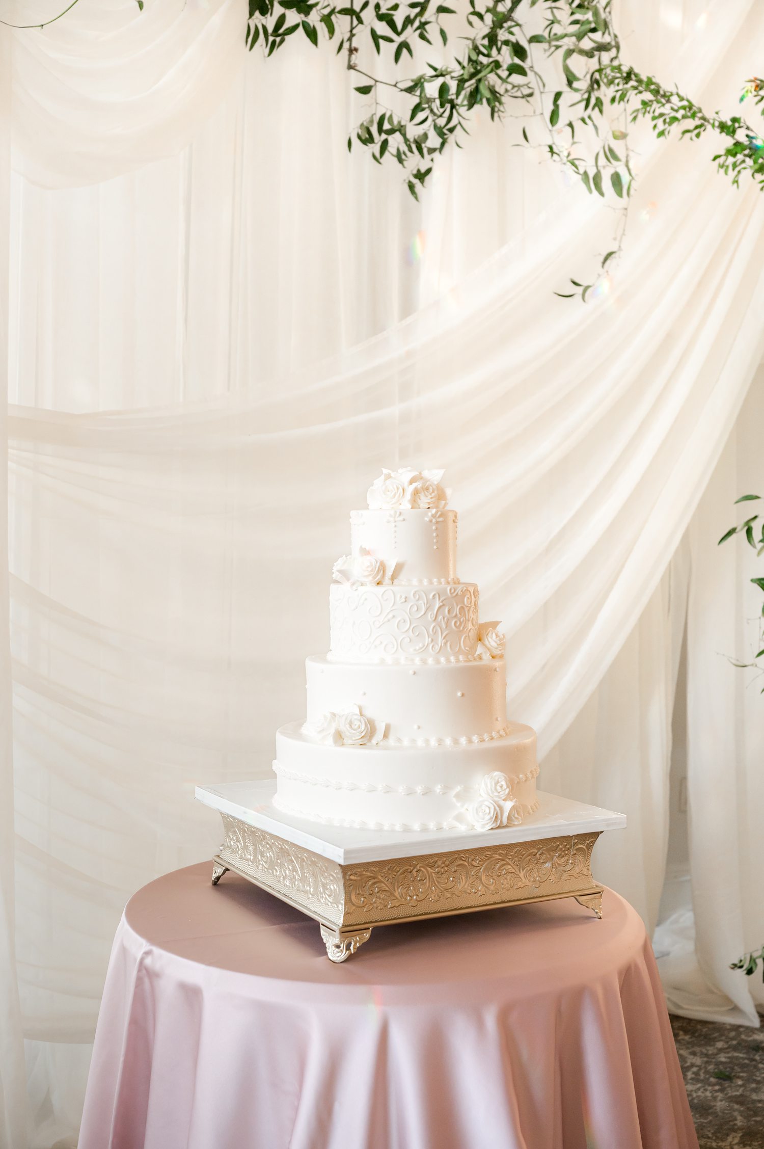 an elegant, classic four-tier round wedding cake finished in smooth white frosting on an ornate gold pedestal stand
