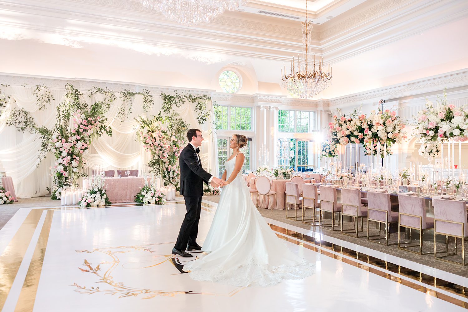 bride and groom during a private moment on a white, custom-monogrammed dance floor in a lavishly dominated by soft, romantic tones of blush pink, white, and gold wedding reception
