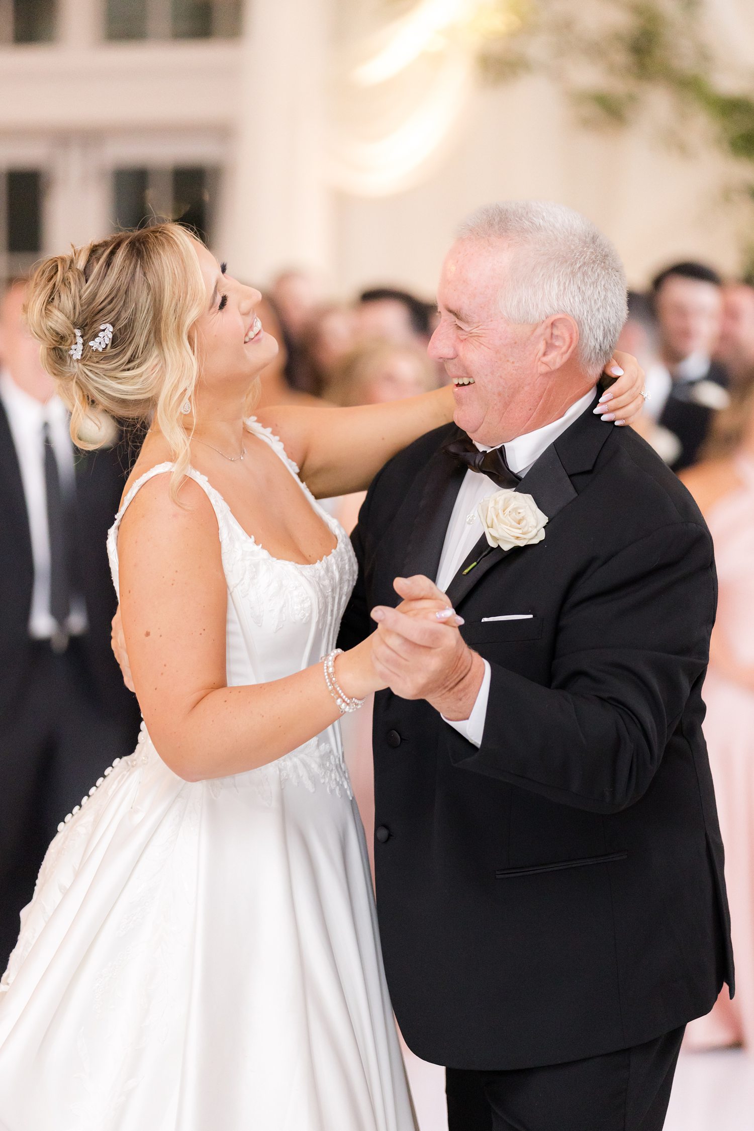  Photo highlighting the bride all smiles while sharing a her first dance with her father surrounded by guests
