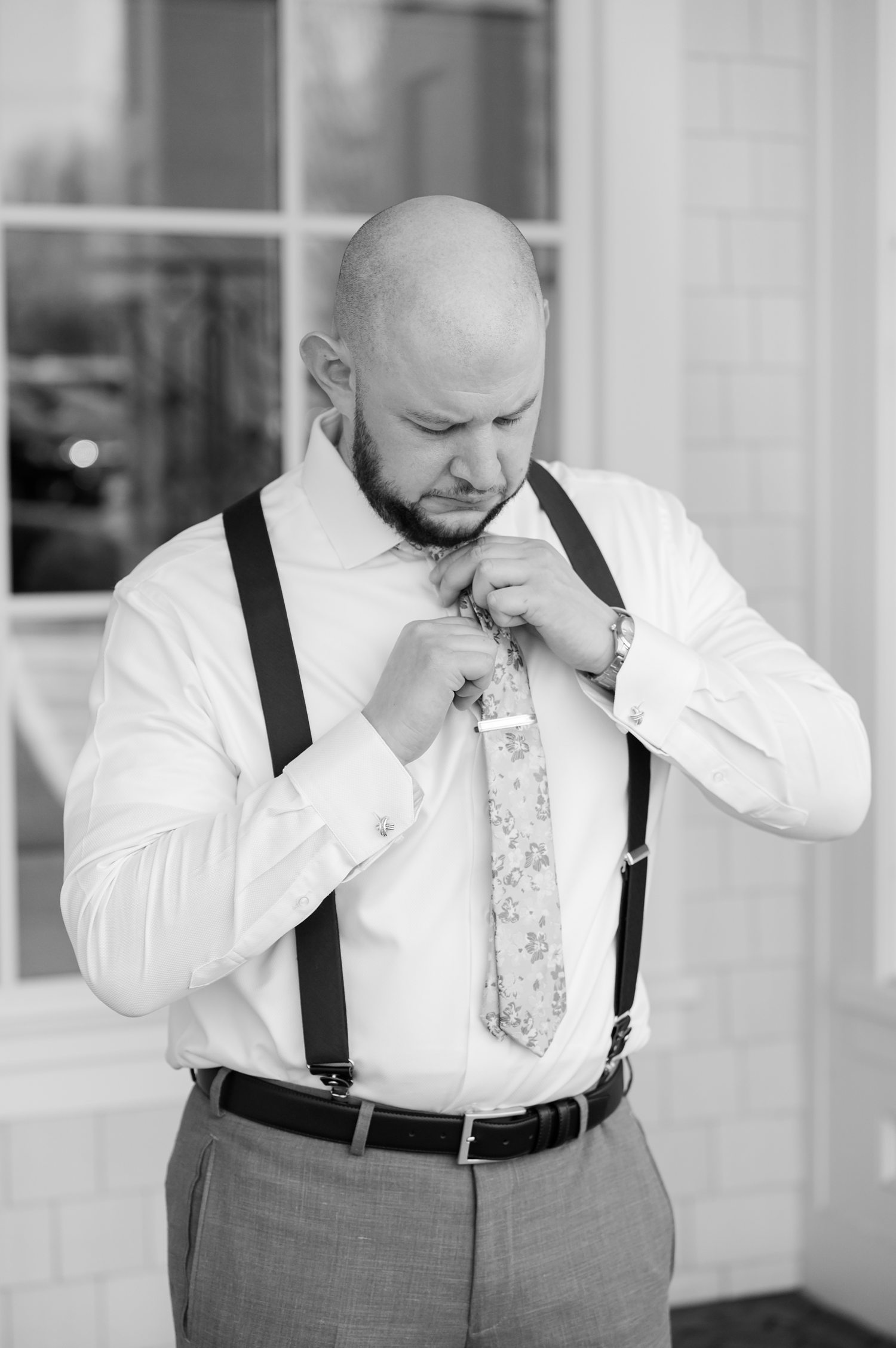 Groom adjusting suspenders in black and white wedding preparation portrait