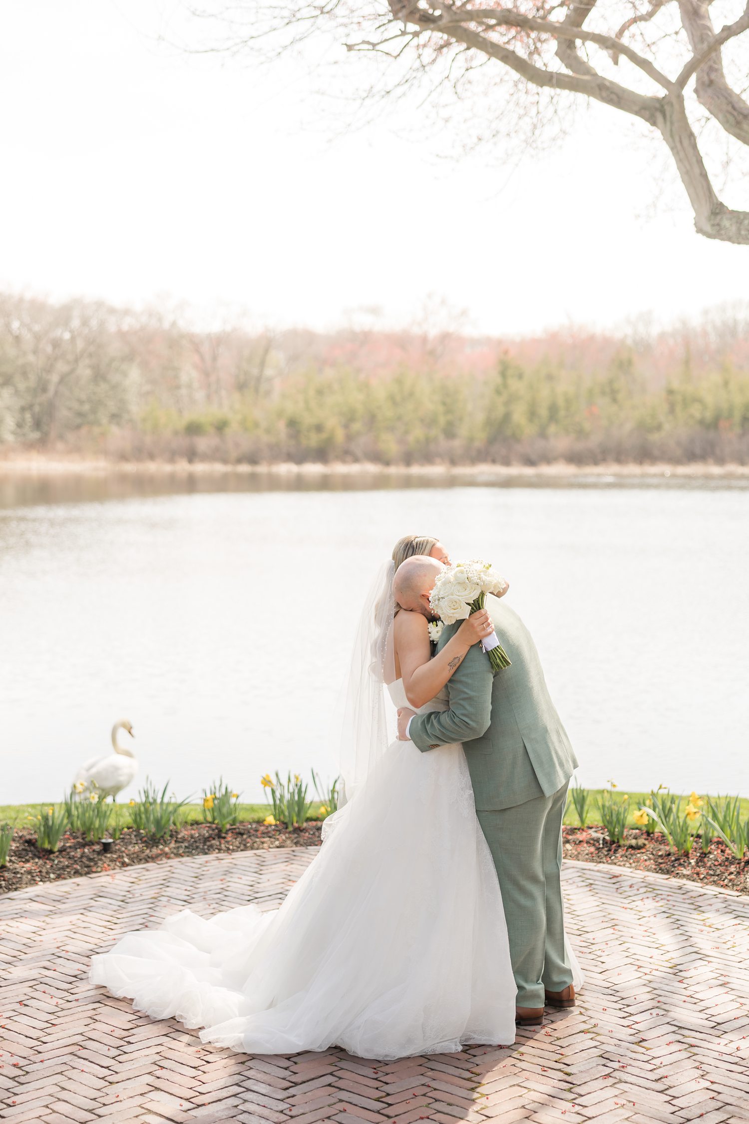 Bride and groom sharing intimate hug beside lakeside manor wedding outdoors