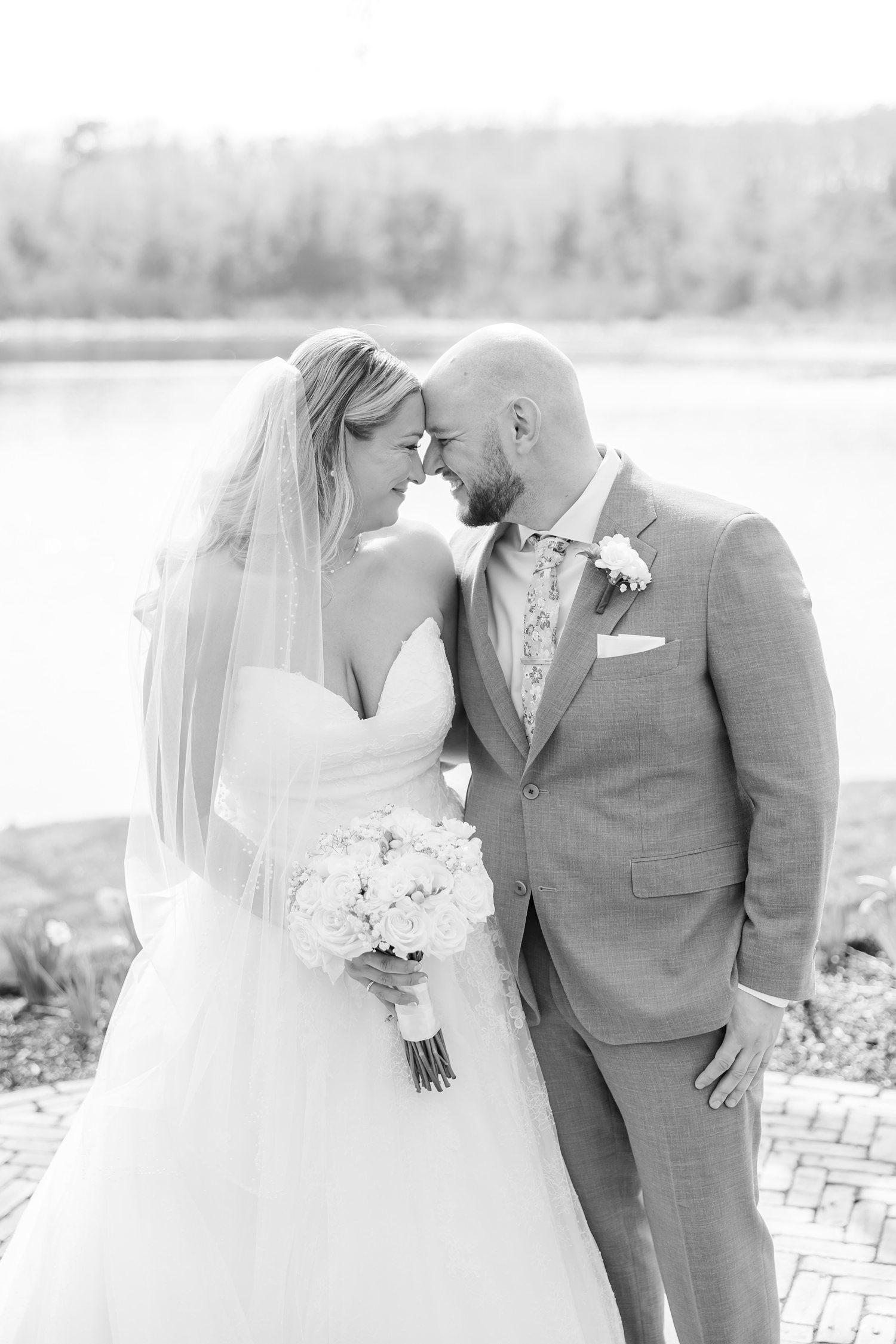 Romantic black and white portrait of bride and groom kissing by the water