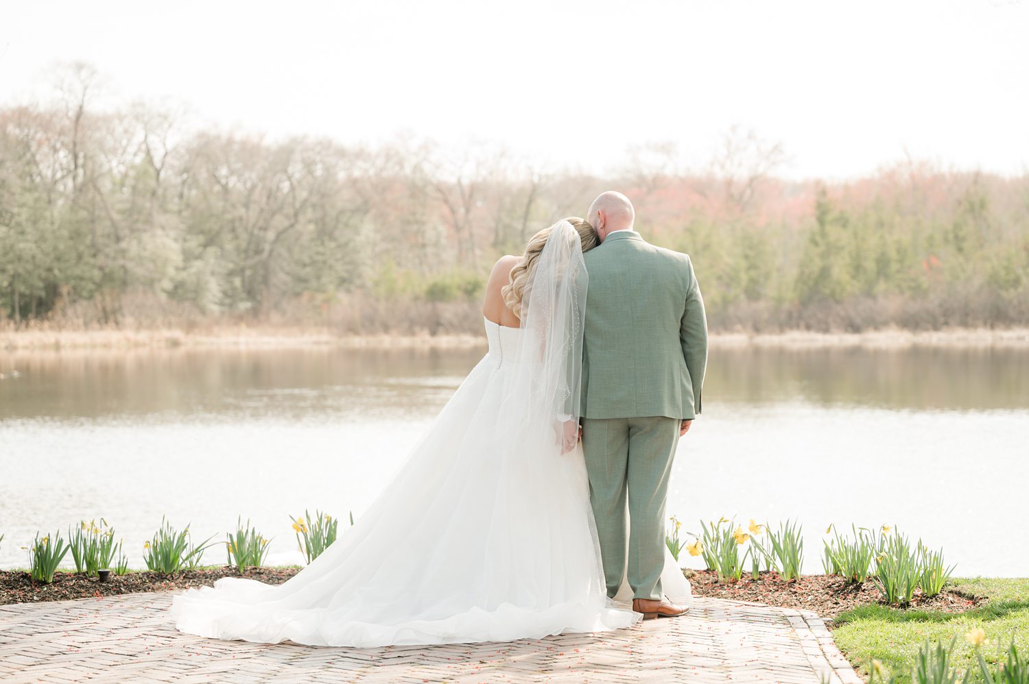 Newlywed couple embracing beside calm lake during sunset wedding session