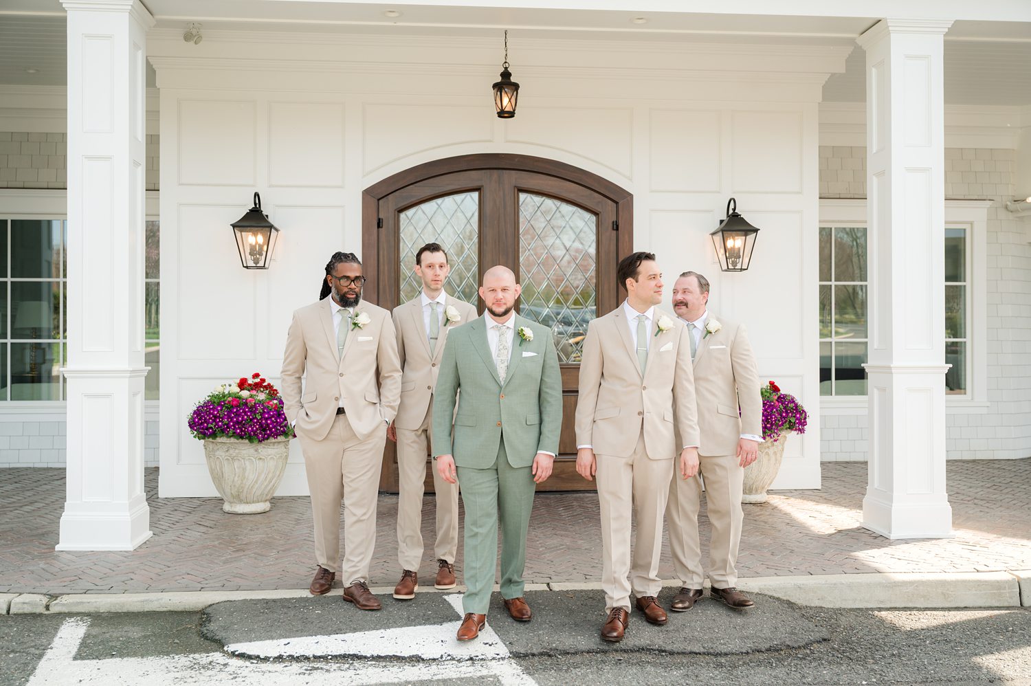 Groomsmen in beige suits posing outside elegant wedding venue entrance
