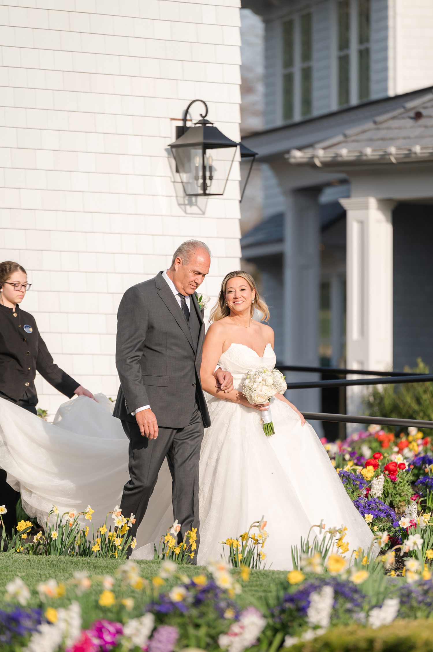 Bride walking with escort through garden path toward outdoor wedding ceremony