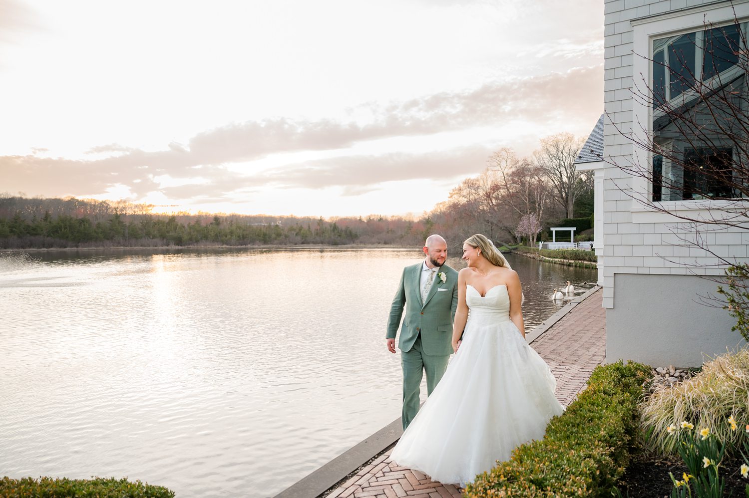 Bride and groom embracing by waterfront during golden hour wedding portraits