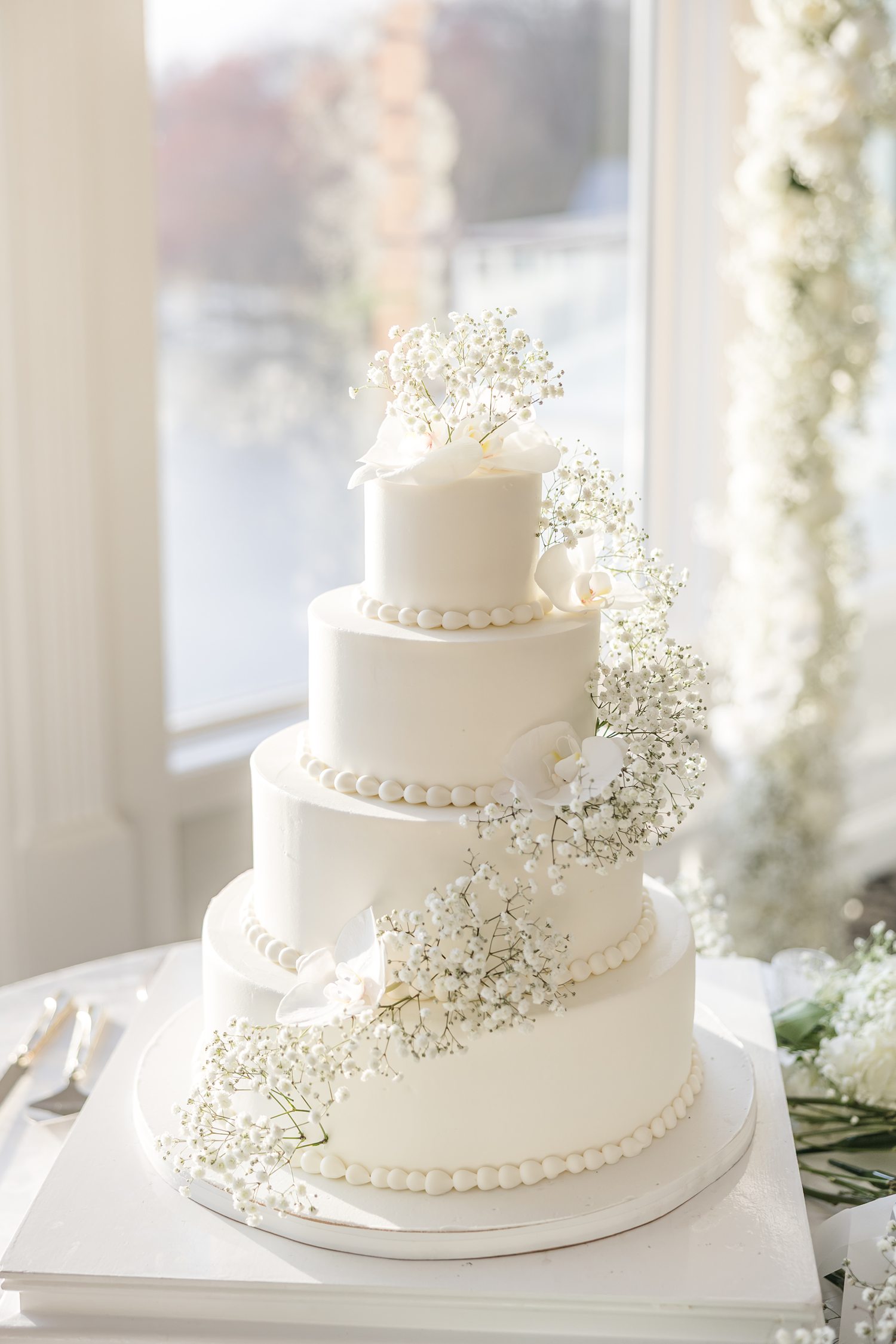 Elegant white multi-tier wedding cake with floral decorations by window