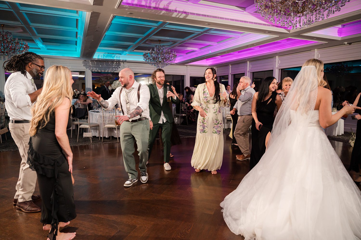 Newlywed couple dancing with guests during elegant ballroom wedding reception