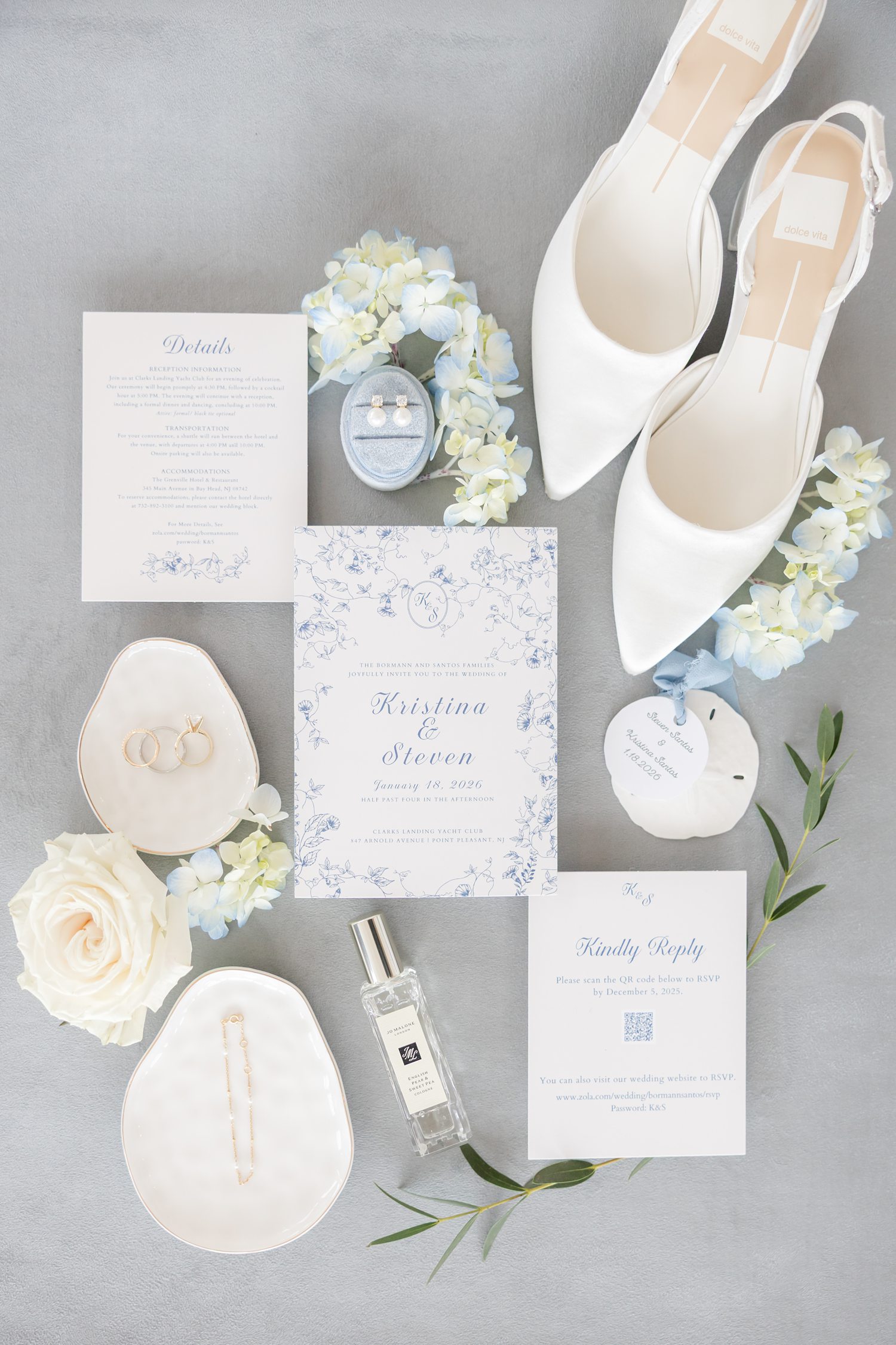 Flat lay of blue and white wedding invitations, rings and bridal details with white and blue florals