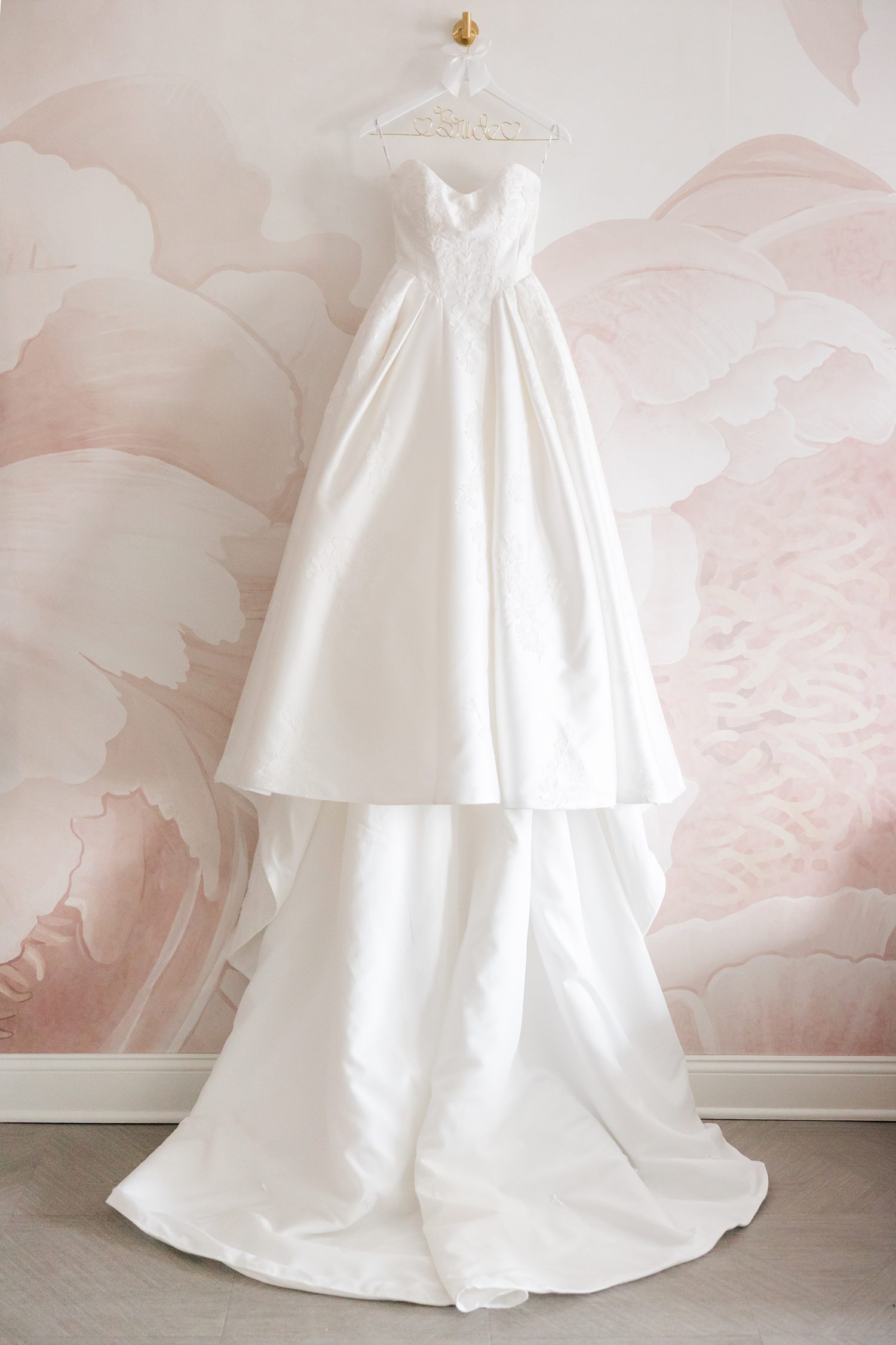 Strapless bridal gown hanging in the getting ready suite against floral pink background