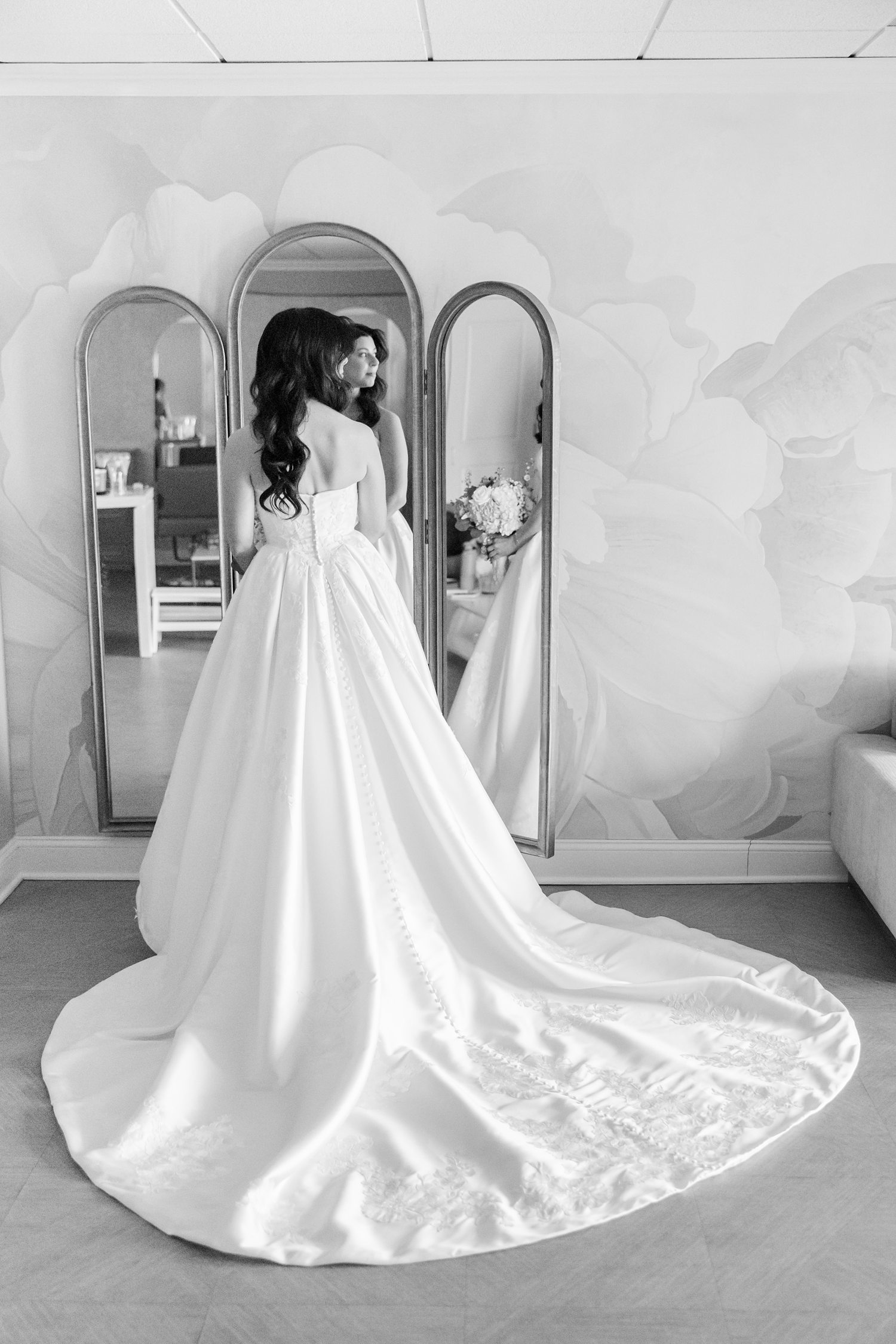 Bride by the mirror holding her bouquet while looking out the window 