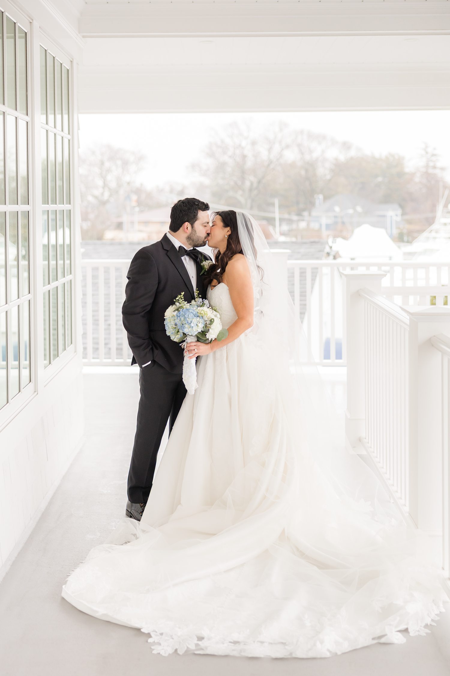 Full body portrait of bride and groom kissing on the balcony while the bride holds her bouquet