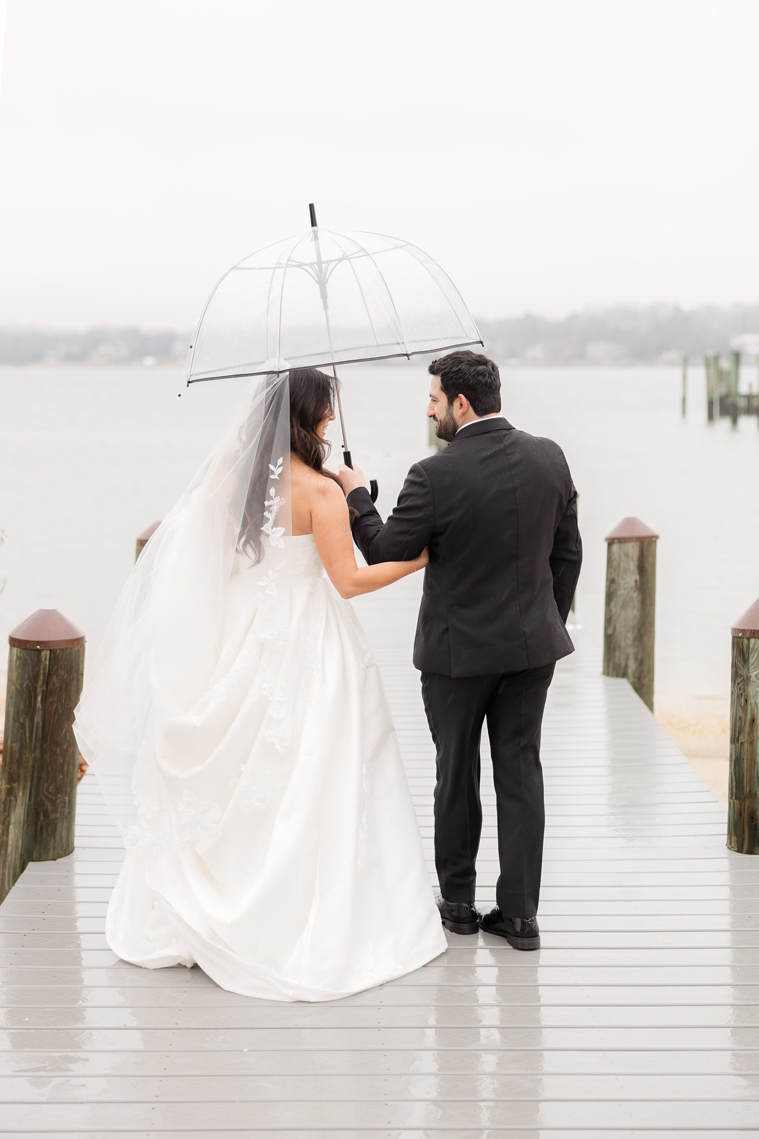 Bride and groom portrait on the rainy waterfront dock under a clear umbrella 