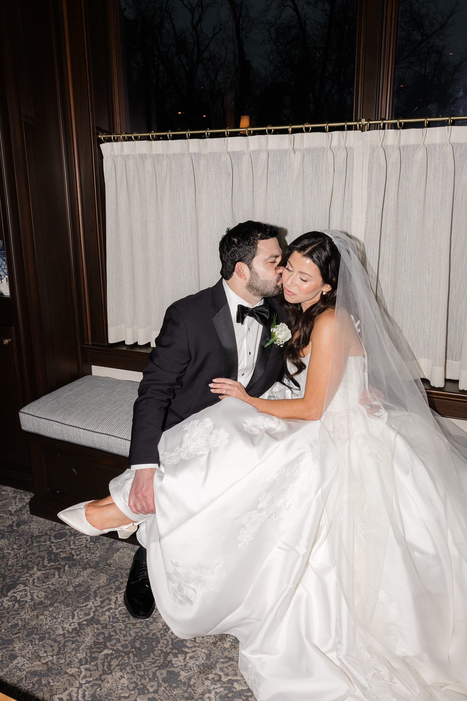 Groom kissing the bride's right cheek while bride's feet is on groom's lap