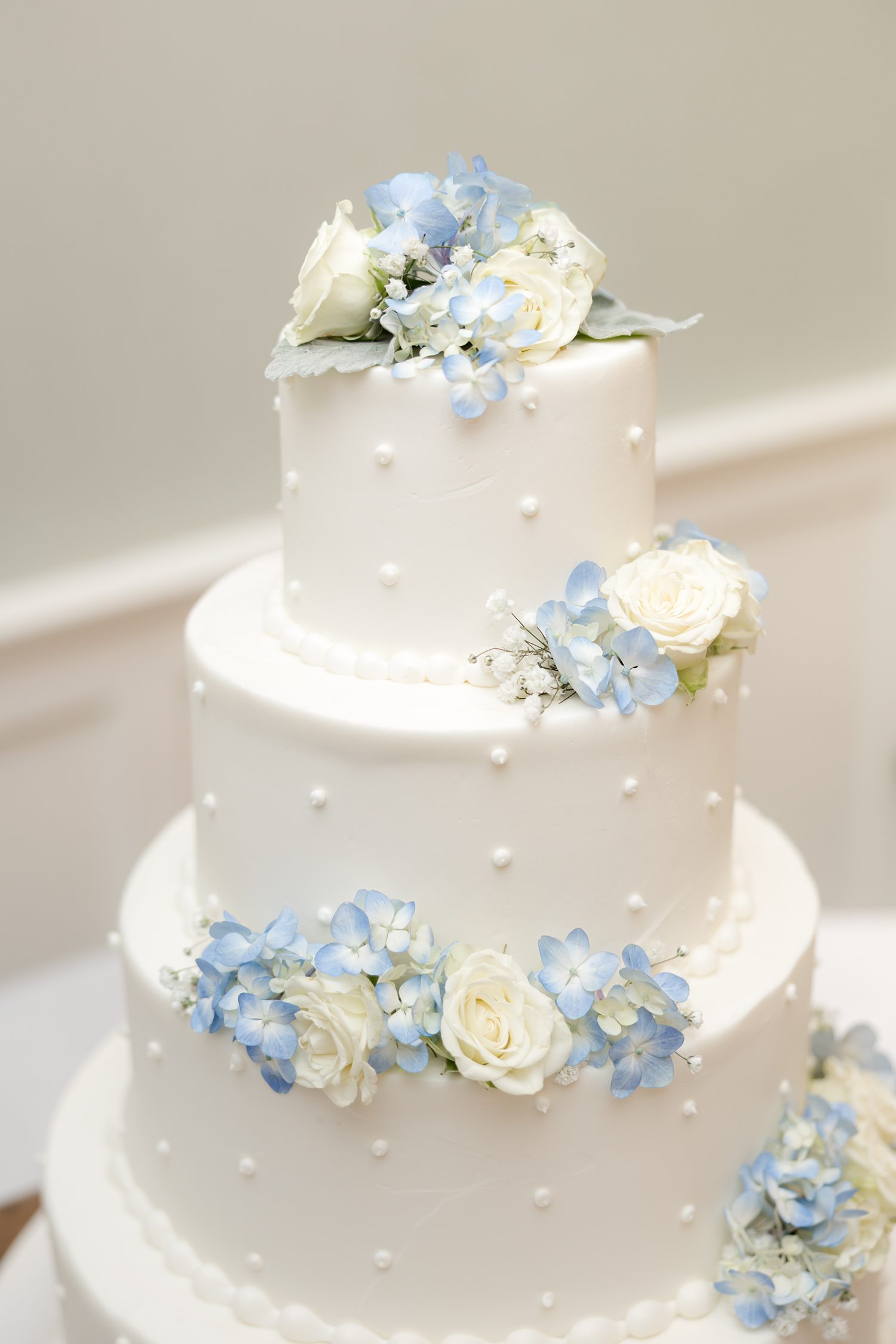 White wedding cake with blue hydrangeas and white roses