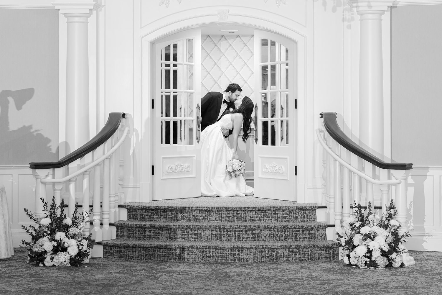 Black and white reception entrance photo of couple kissing on the venue steps