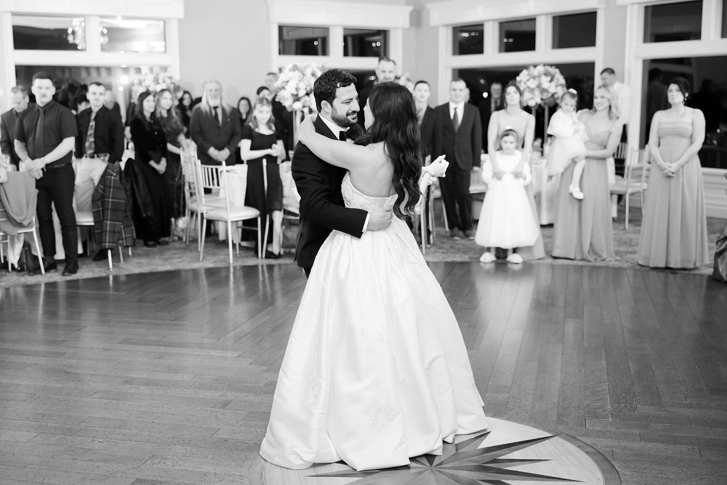 Black and white first dance photo of the bride and groom with guests watching
