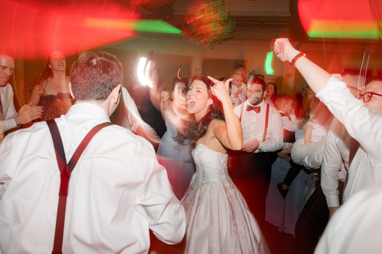 Guests surrounding bride and groom while dancing under colorful reception lights at Clarks Landing Yacht Club 