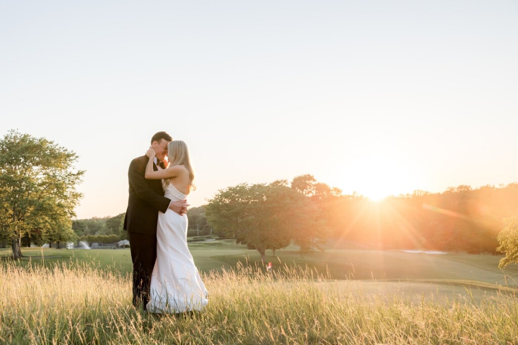 Newlywed kiss in a field at sunset