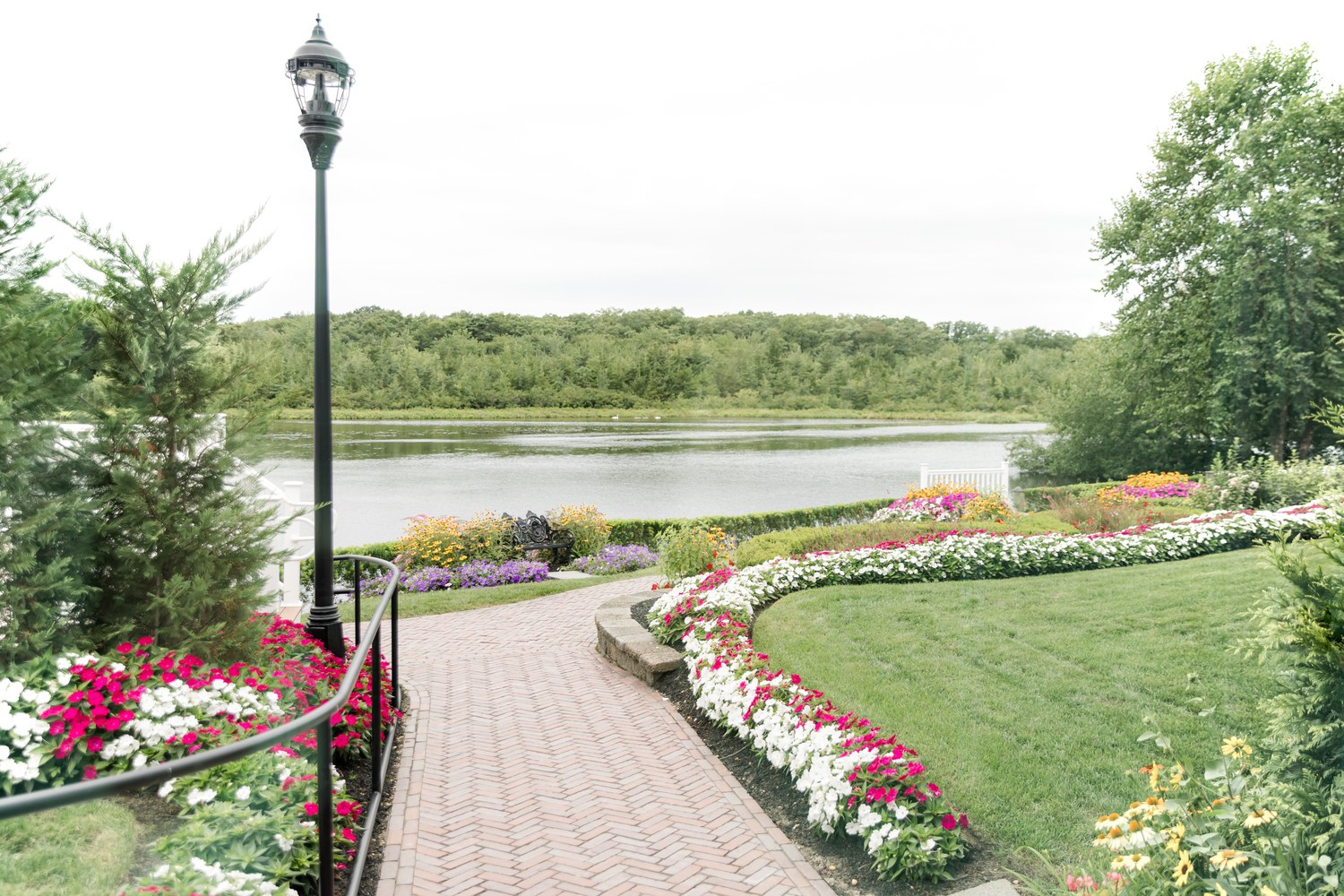 Flower-lined brick walkway leading to the lake at The Mill Lakeside Manor wedding venue