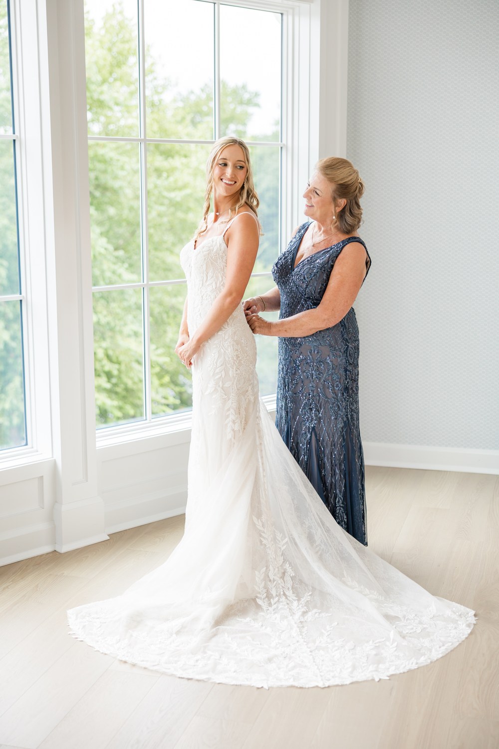 Mother of the bride helping the bride into her lace wedding gown at The Mill Lakeside Manor