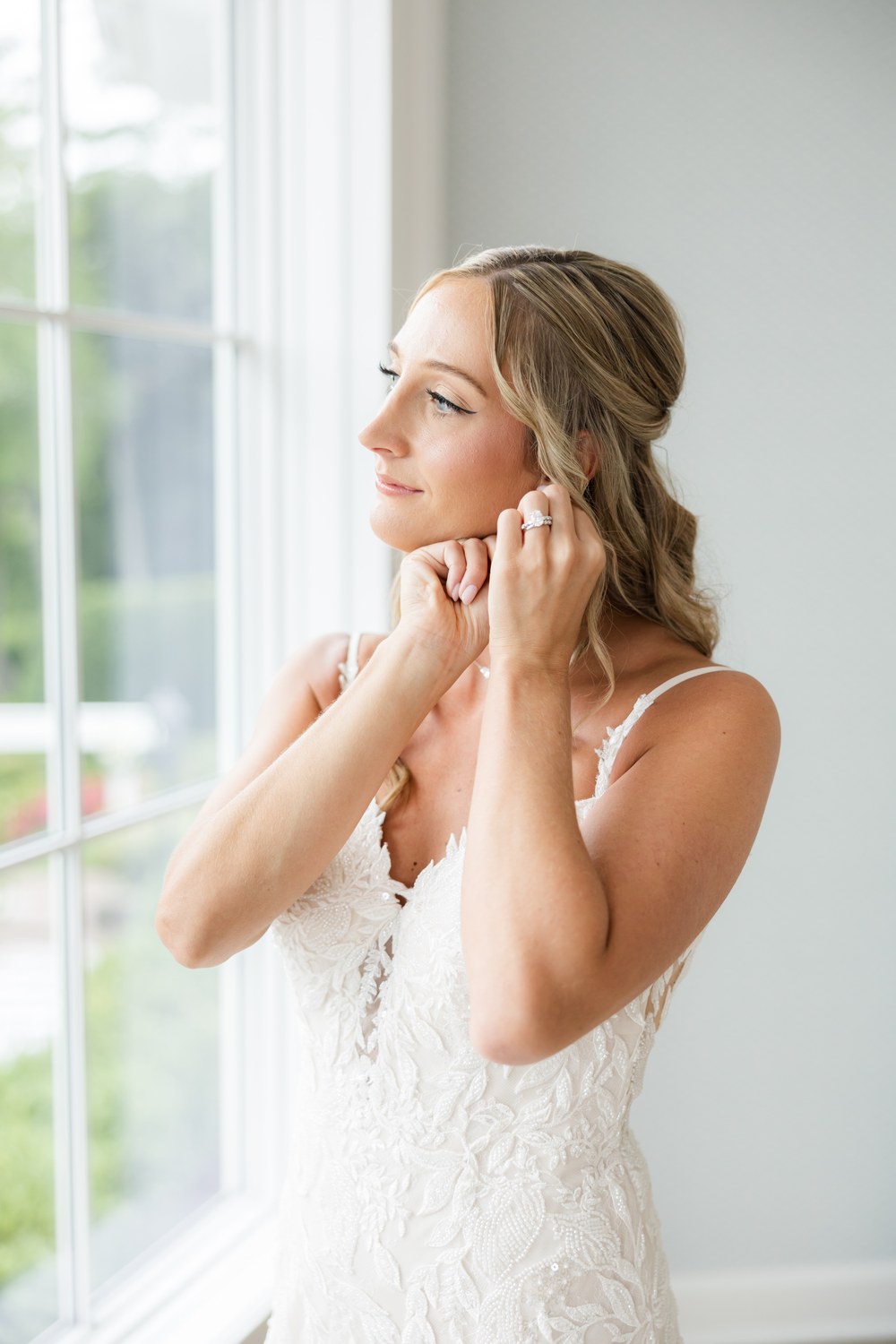 Bride fastening her earring in a bright window at The Mill Lakeside Manor