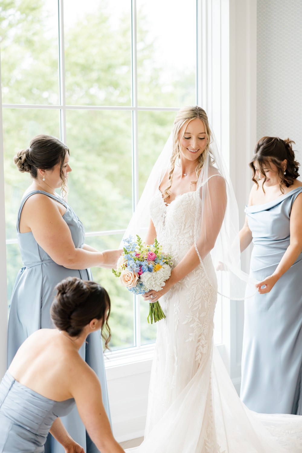 Bride laughing with her bridesmaids in dusty blue dresses at The Mill Lakeside Manor