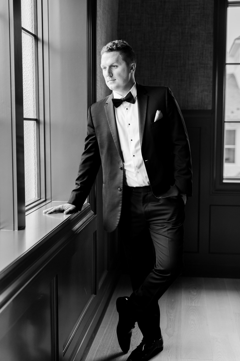 Black and white portrait of the groom leaning at a window