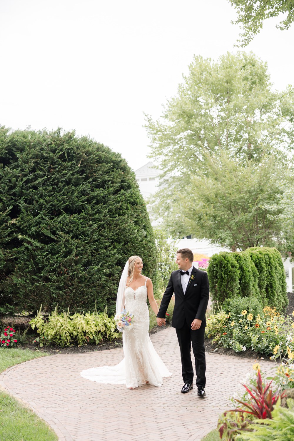 Bride and groom walking hand in hand along a brick garden path