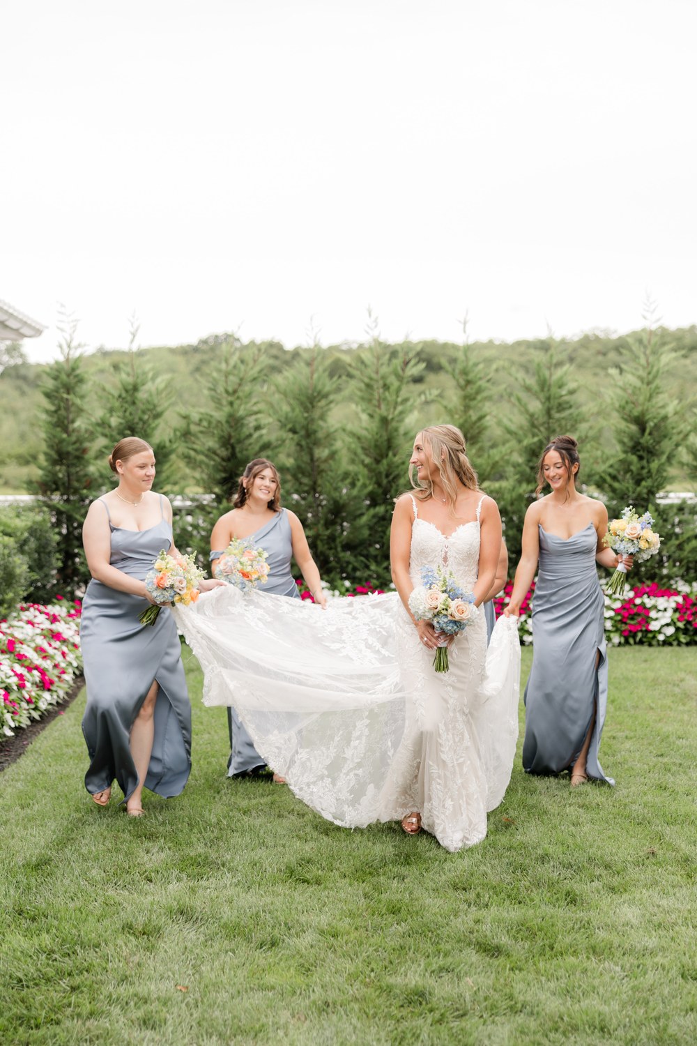 Bridesmaids holding the bride's dress on the lawn at The Mill Lakeside Manor