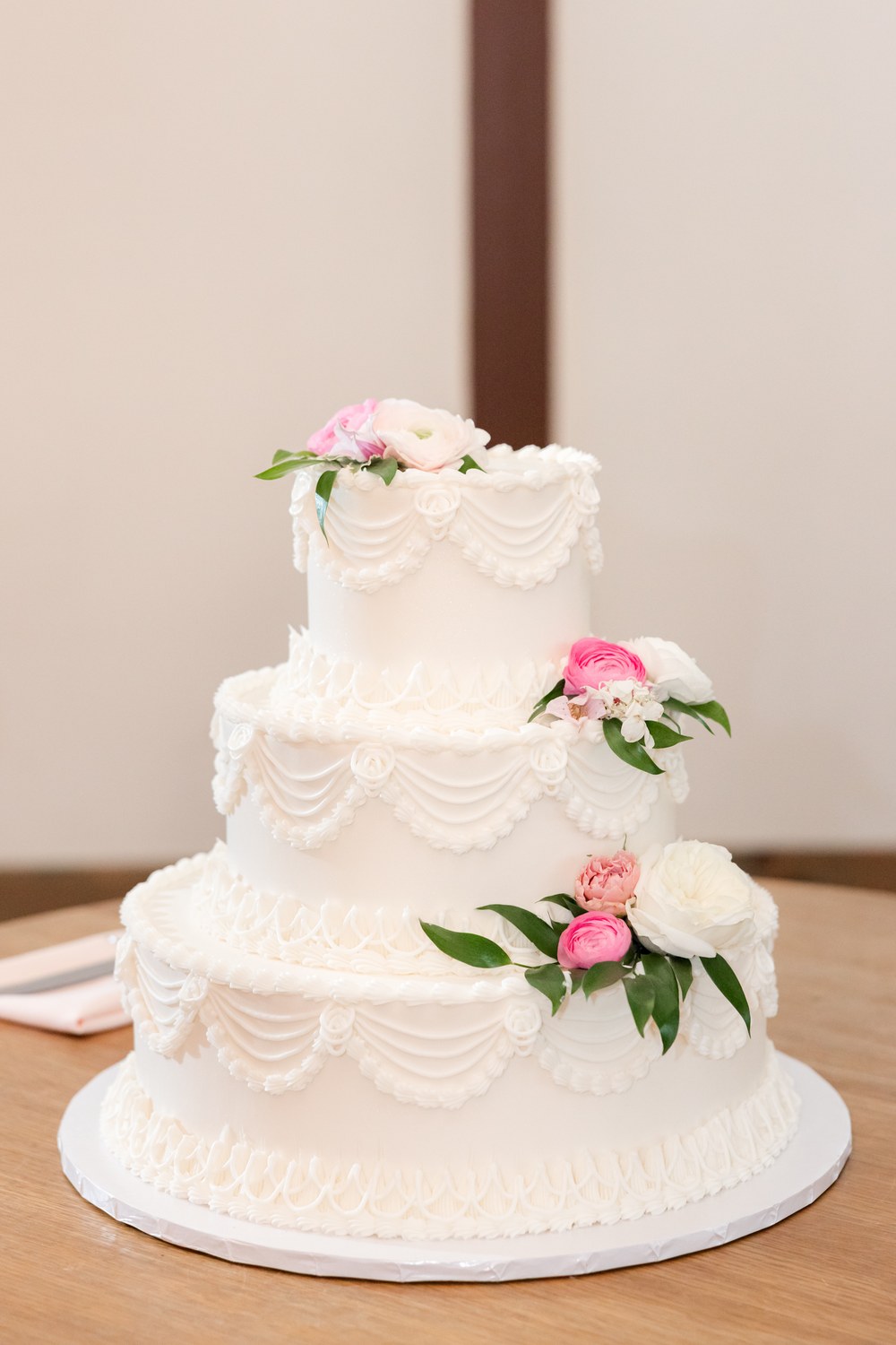 Three-tier white wedding cake with pink flowers