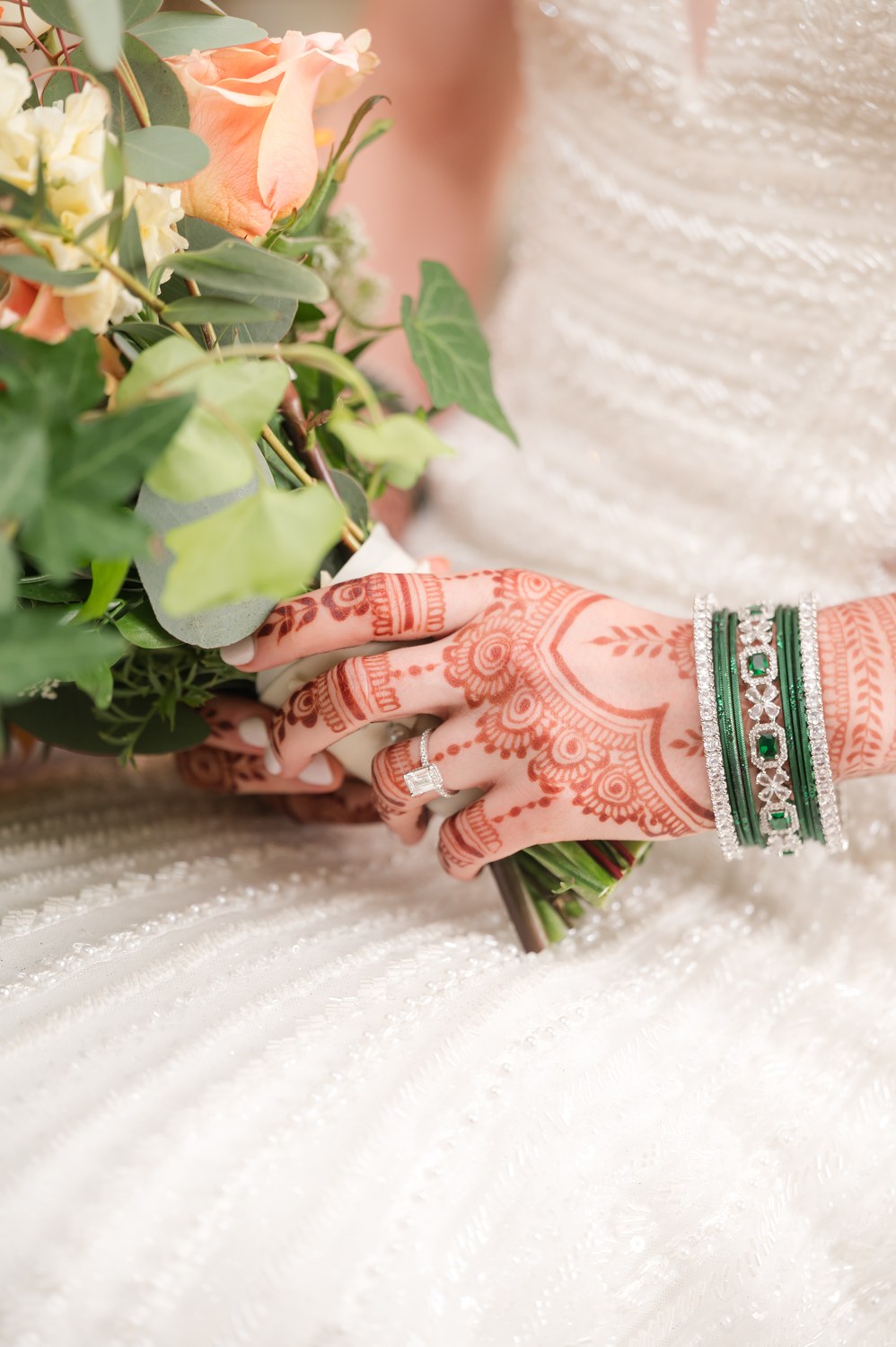 Bride's henna-decorated hands holding her orange and white bridal bouquet