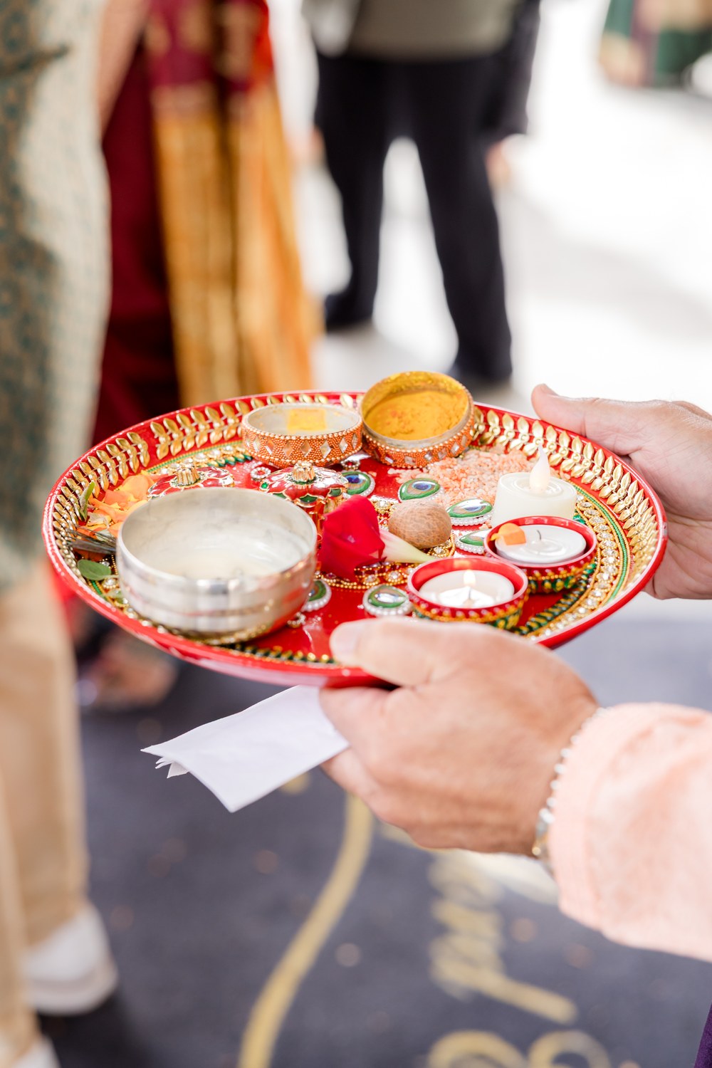 Hands holding a decorated aarti thali for the groom's welcome ritual